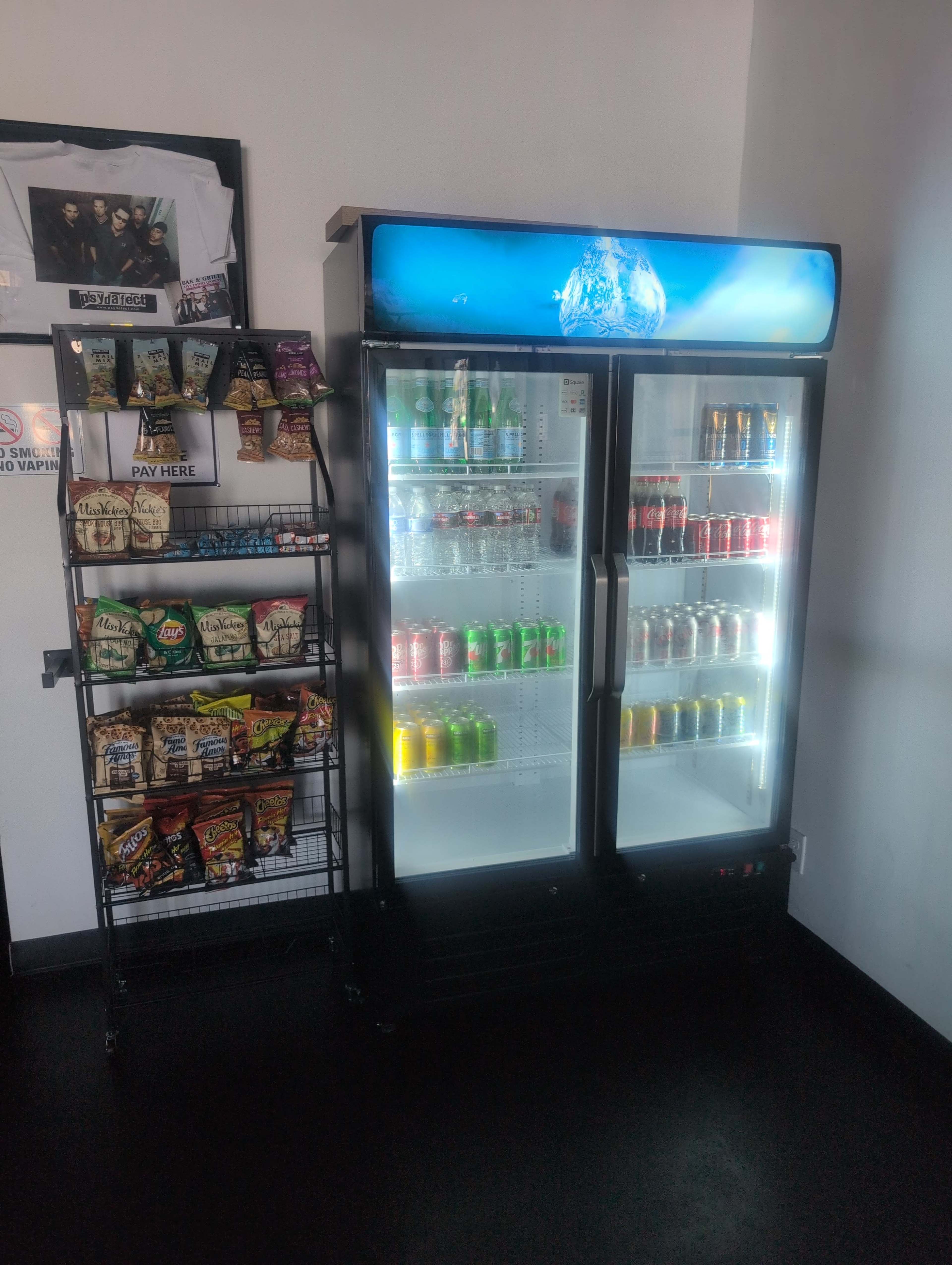 The image shows a drink refrigerator filled with various beverages next to a rack displaying a selection of snacks.