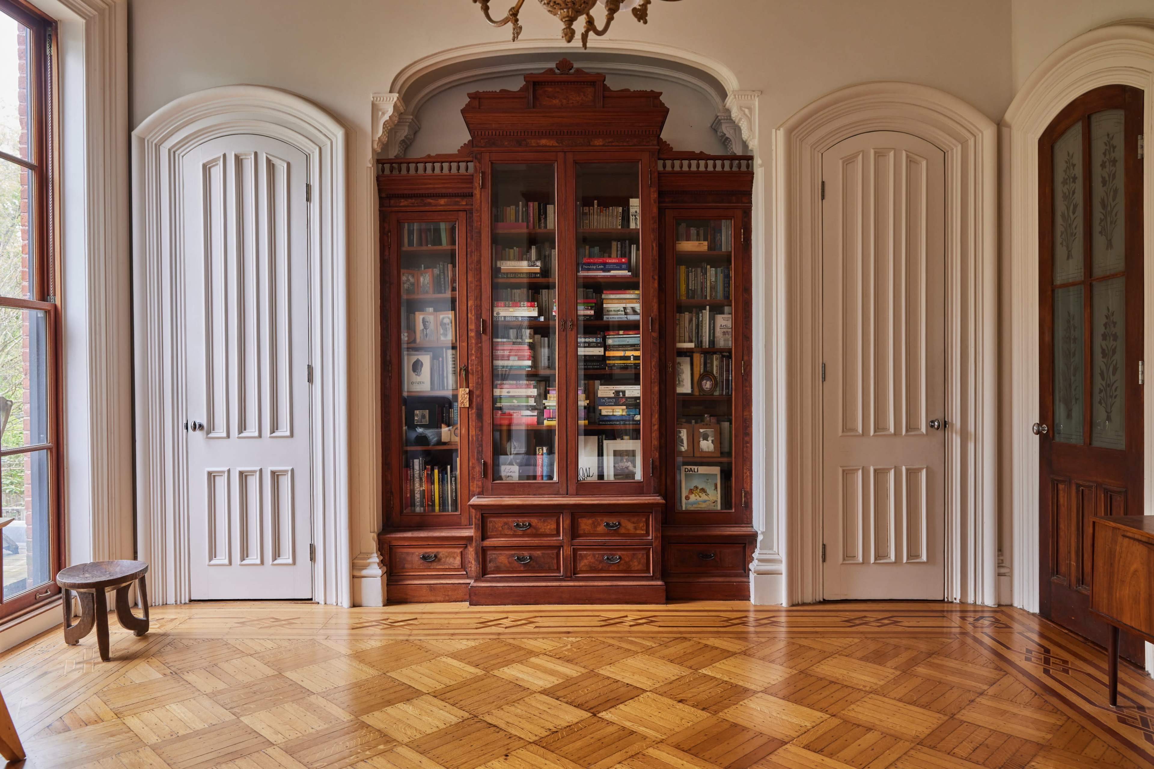 The image shows a room with wooden flooring featuring a large, ornate bookshelf centered between two doors.