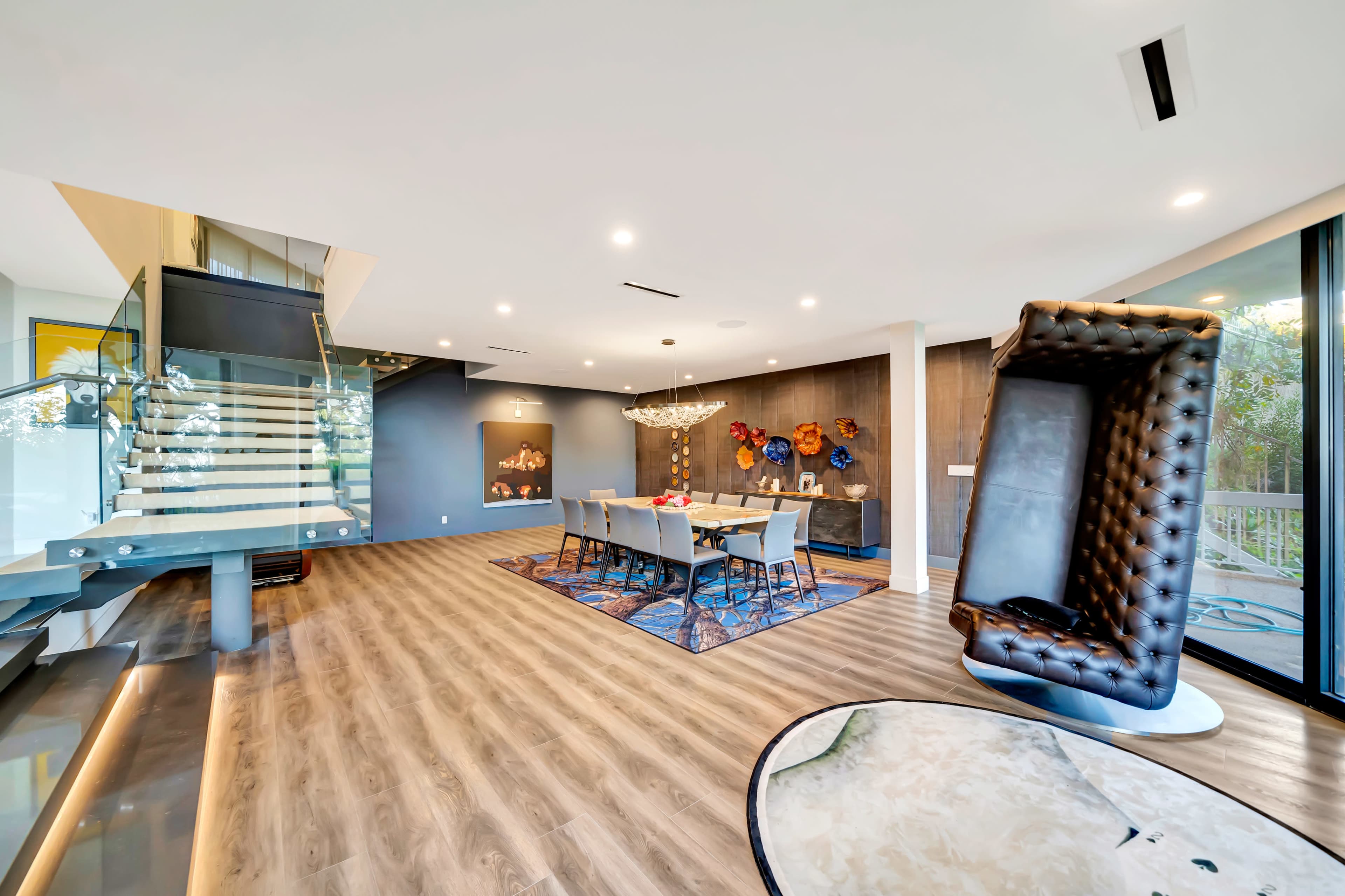 A modern interior space features a dining area with a large table and stylish chairs, surrounded by contemporary decor and a staircase leading to an upper level.