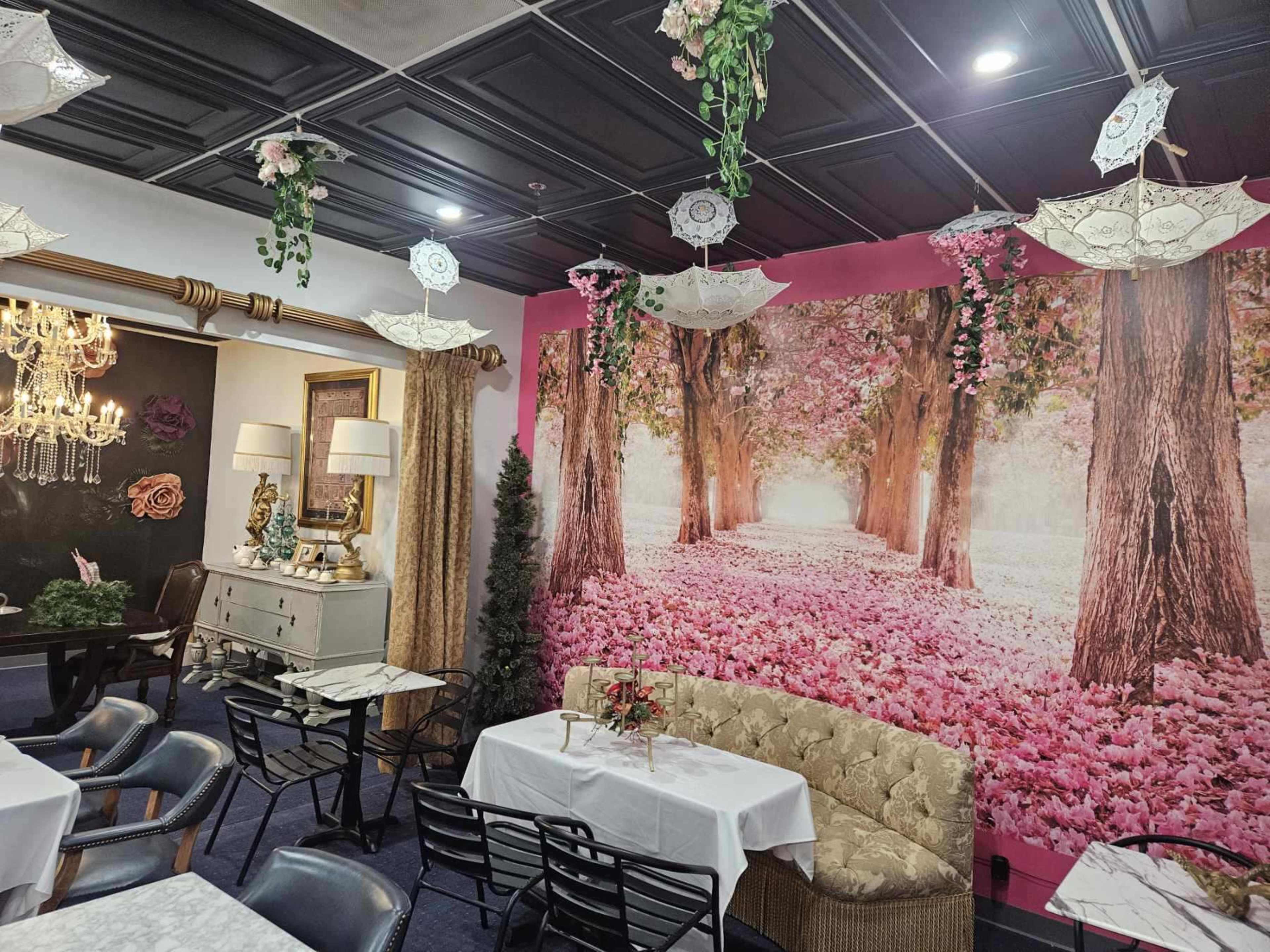 A restaurant interior featuring a mural of a tree-lined path with pink flowers, complemented by decorative umbrellas hanging from the ceiling.