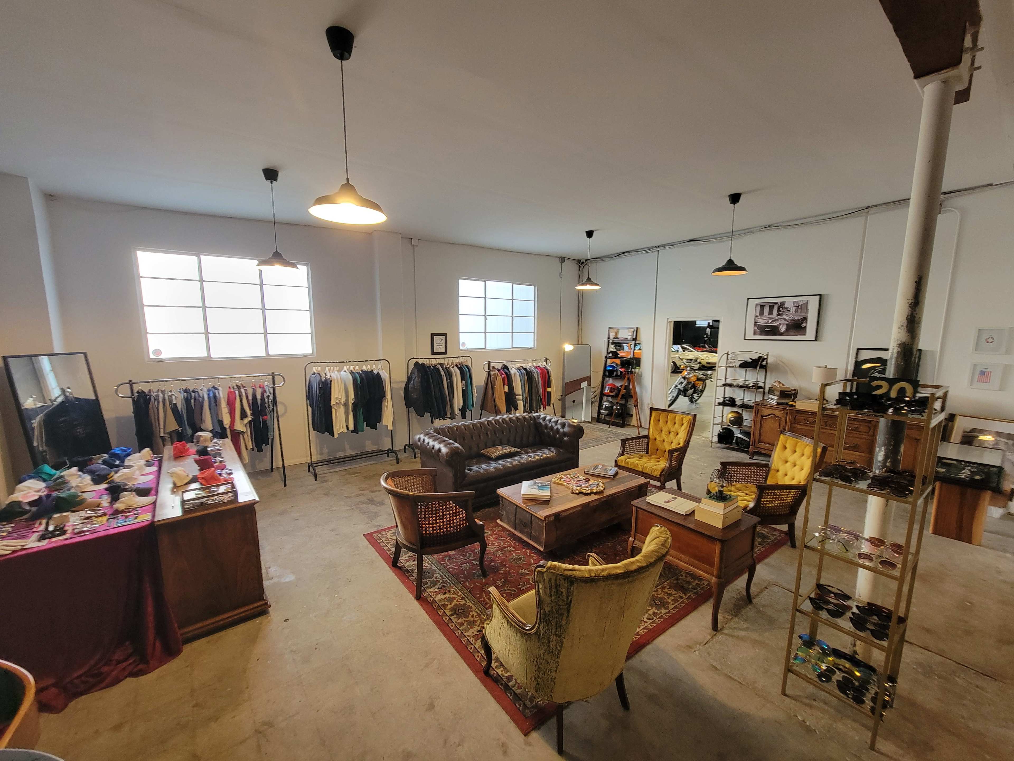 The image shows a vintage-style boutique with racks of clothes, a cozy seating area featuring a leather sofa and armchairs, and various displays of accessories and decor.