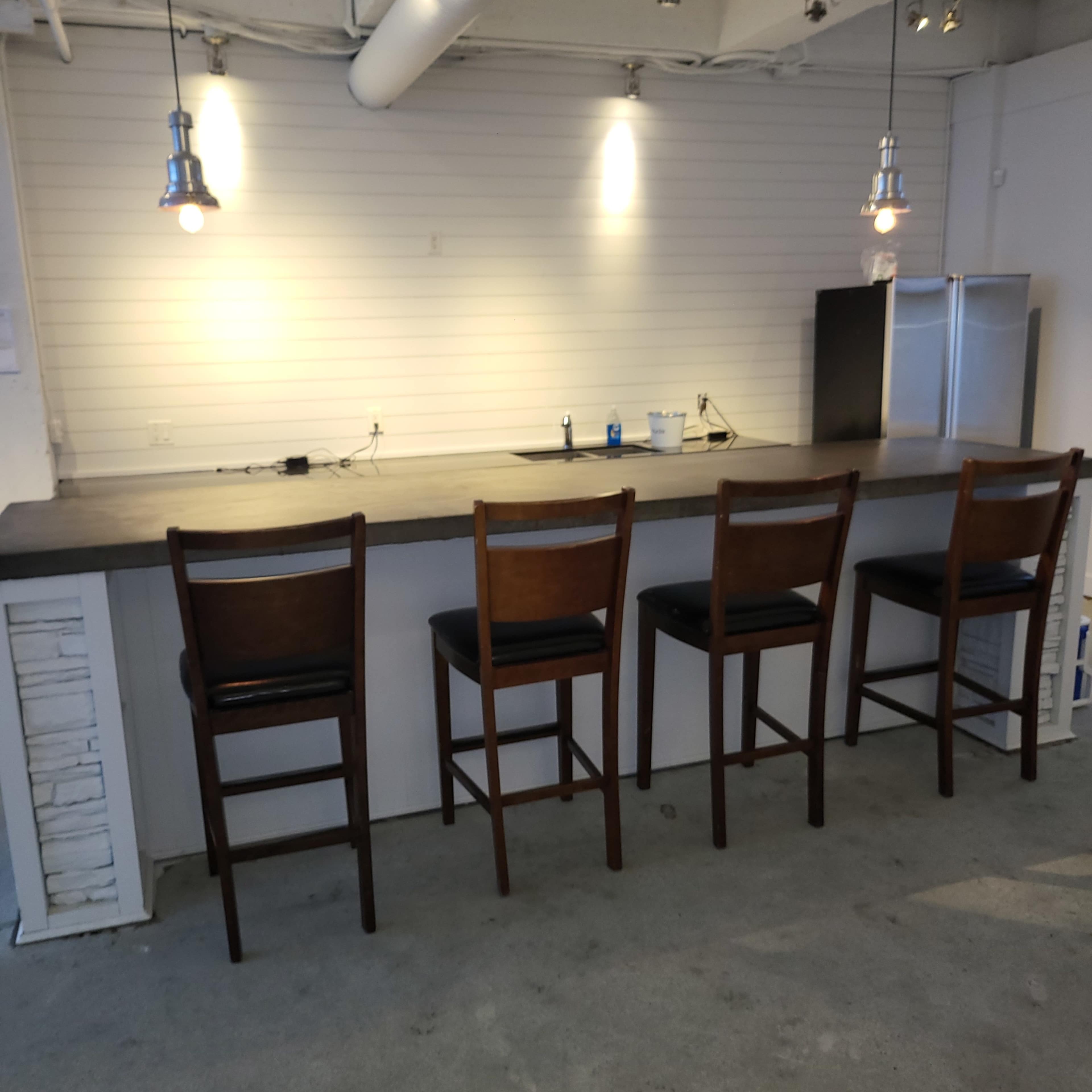 A modern bar area features a countertop with four wooden stools and industrial-style pendant lighting above.
