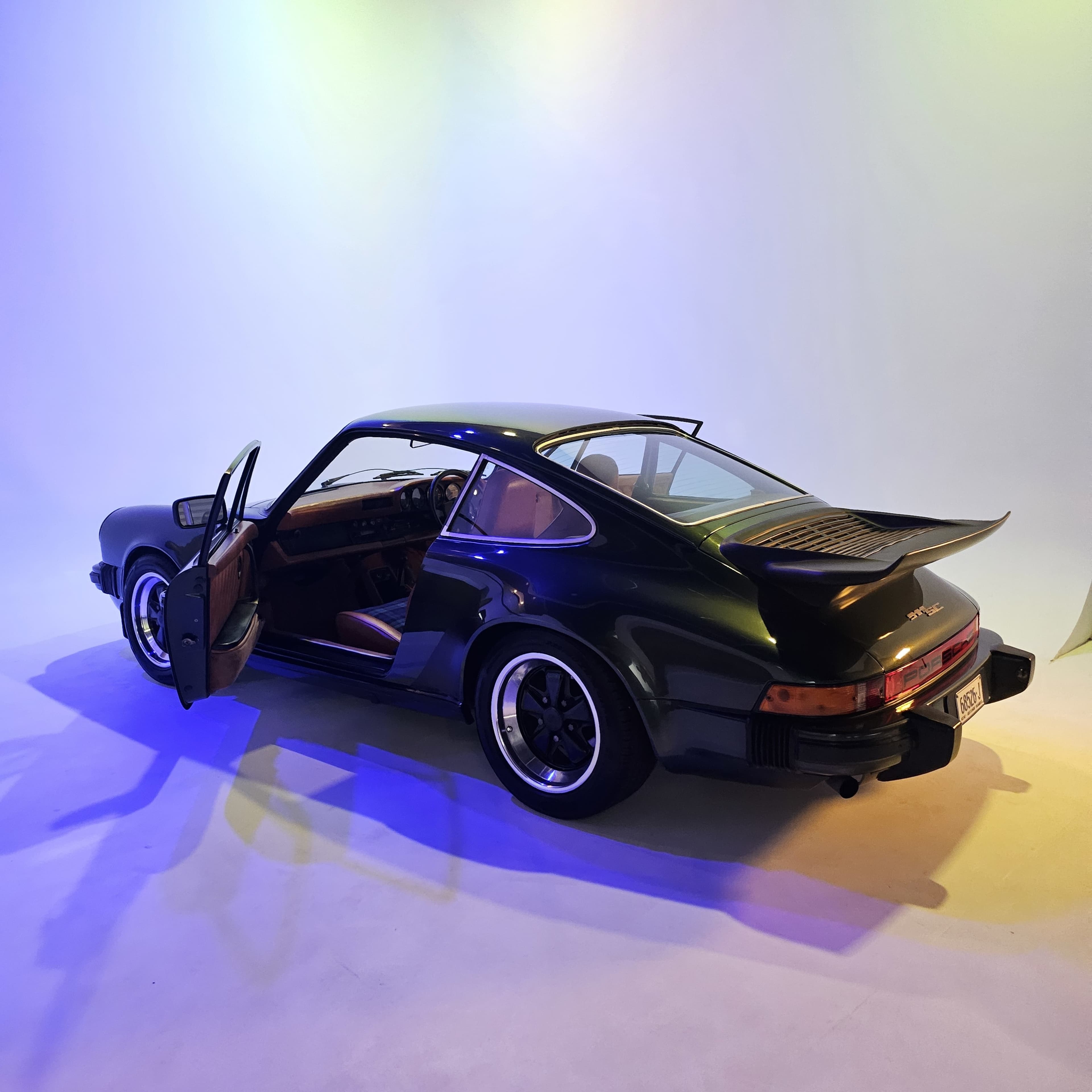 A vintage sports car with an open door is positioned against a softly lit, colorful backdrop.