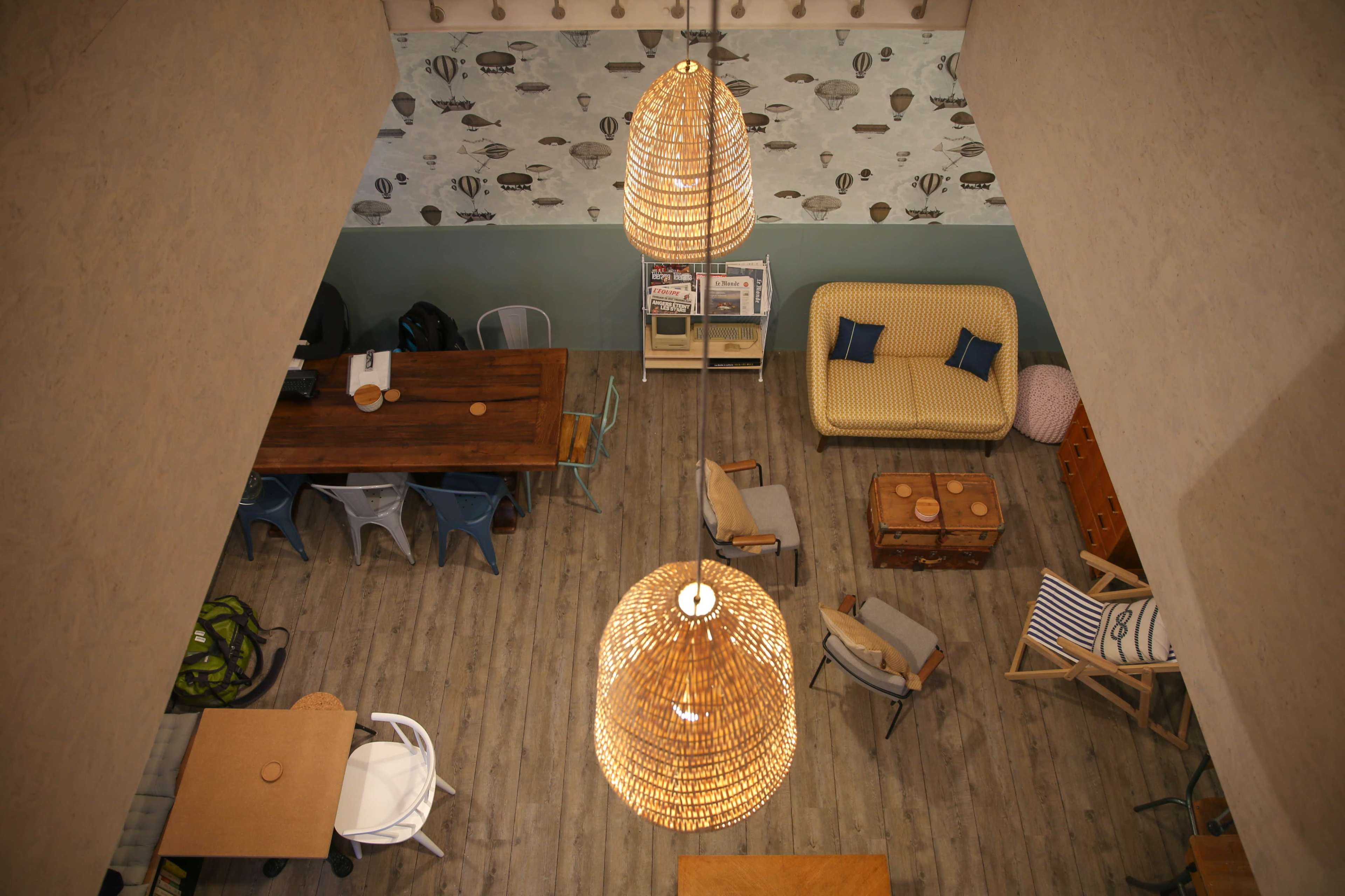 An interior of a cafe with wooden and metal furniture, two large woven pendant lights, and a patterned wall featuring balloons.