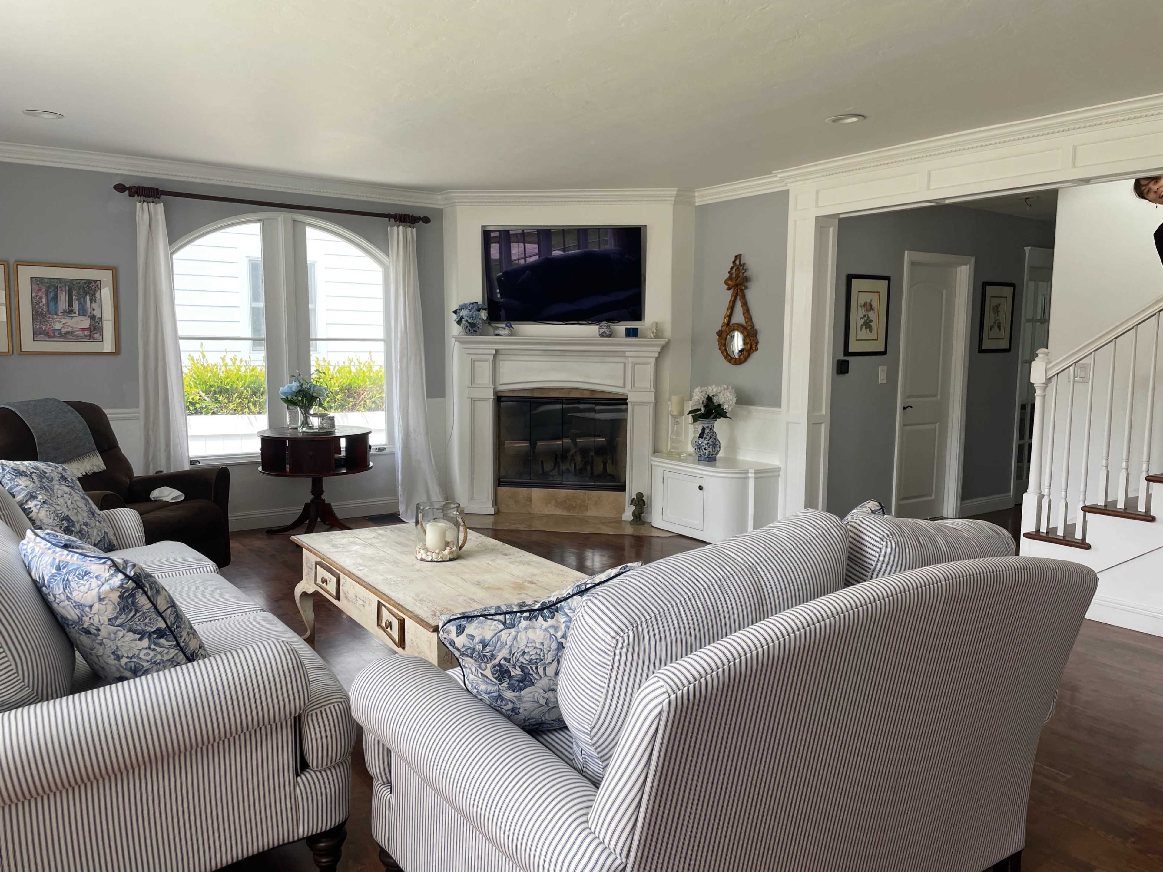 A spacious living room features a large sofa and armchairs arranged around a coffee table, with a fireplace and a television mounted above it.