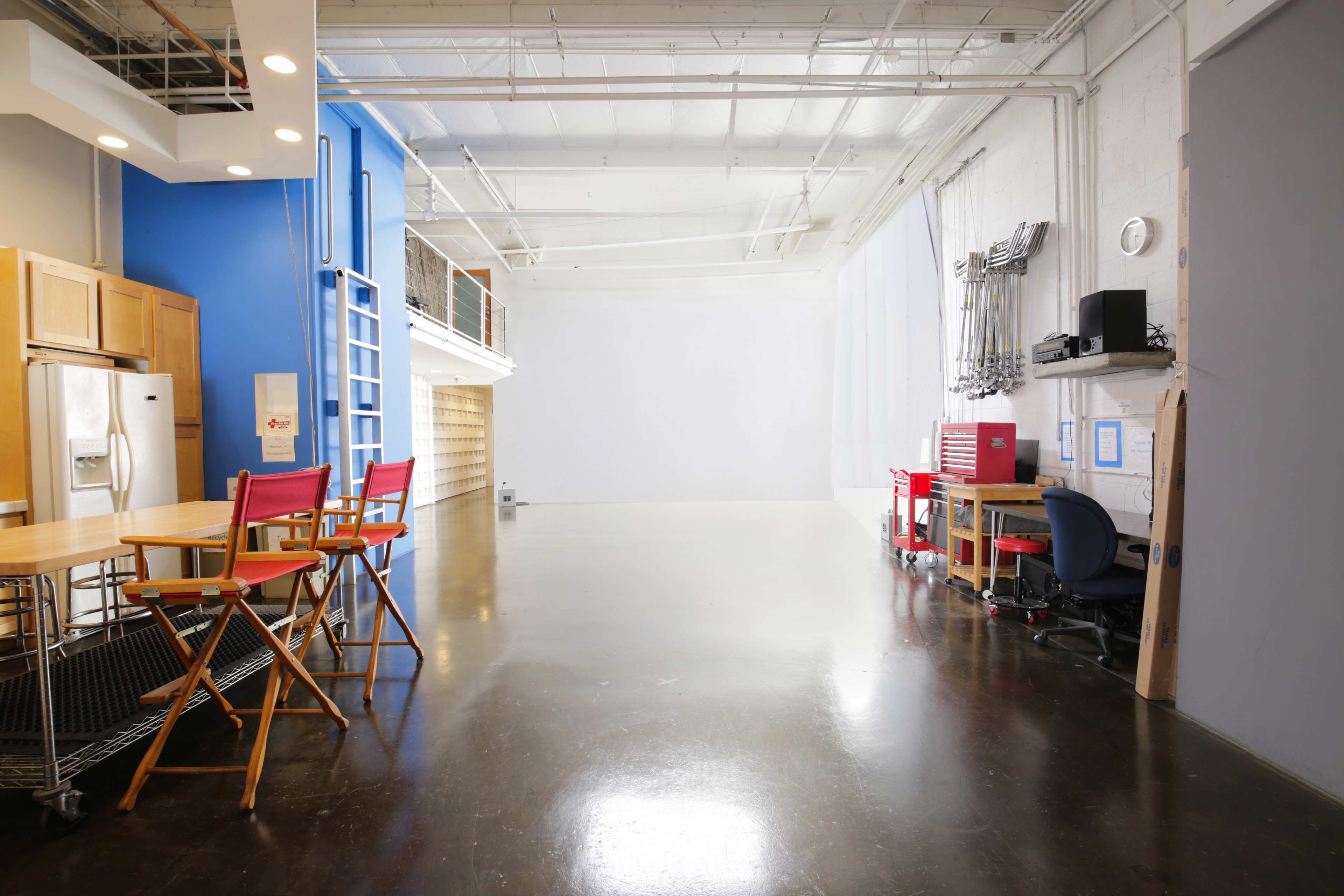 A spacious, open studio with a kitchen area on the left and a blank wall on the right.