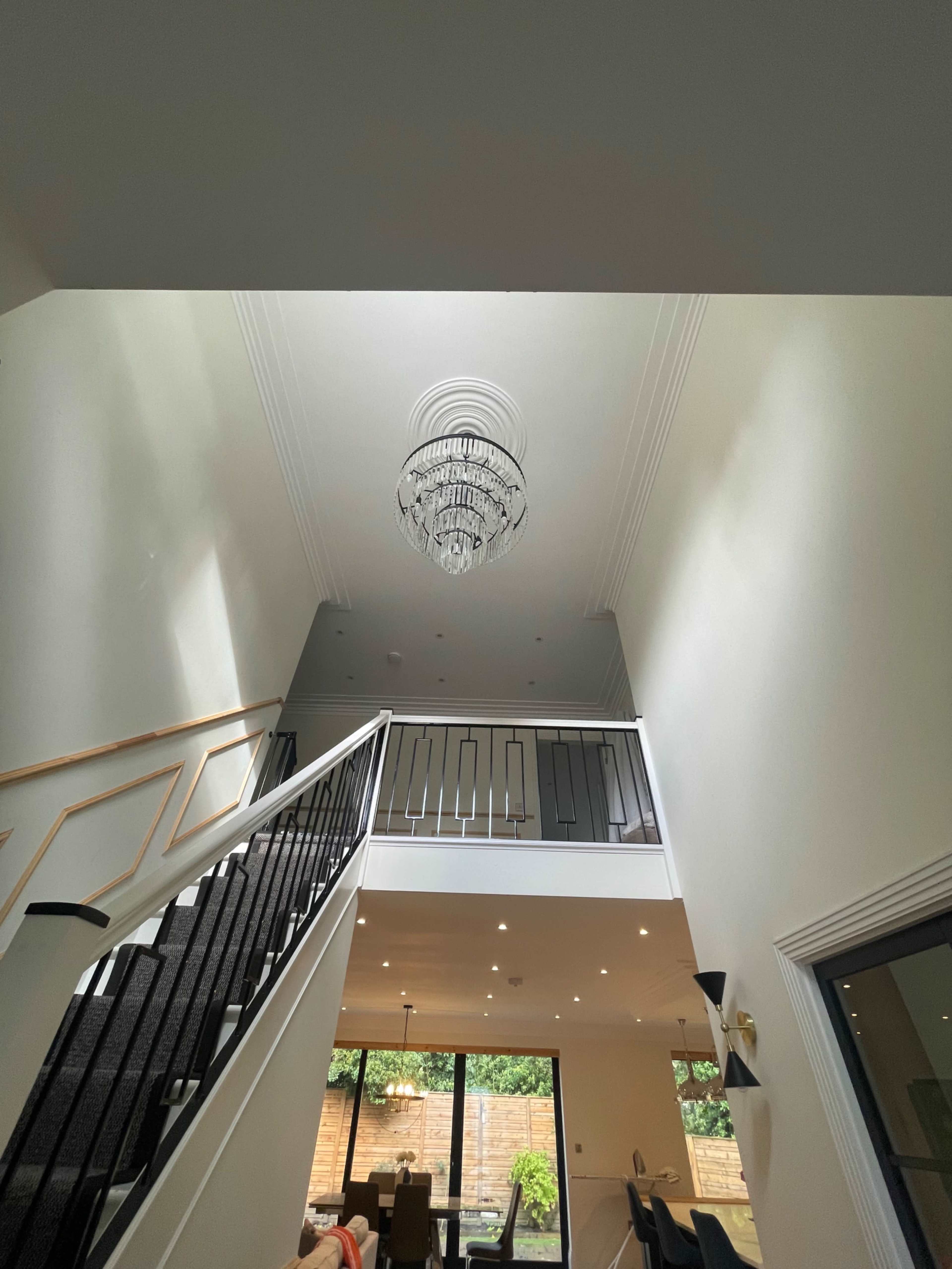 The image shows a bright stairwell with a chandelier hanging from the ceiling and a view of a modern open space below.