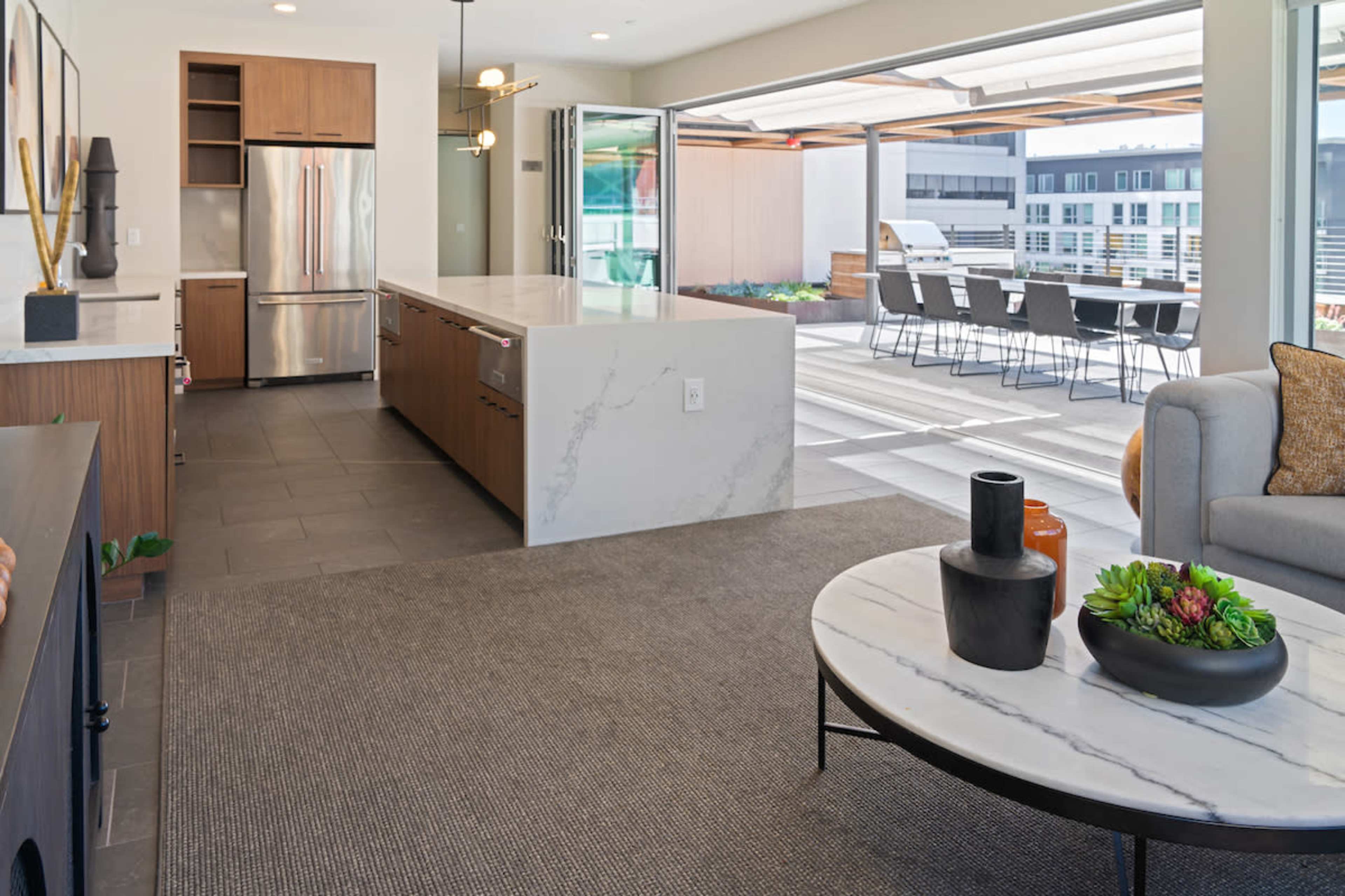 The image shows a modern open-concept kitchen and living area leading to a patio with outdoor seating.