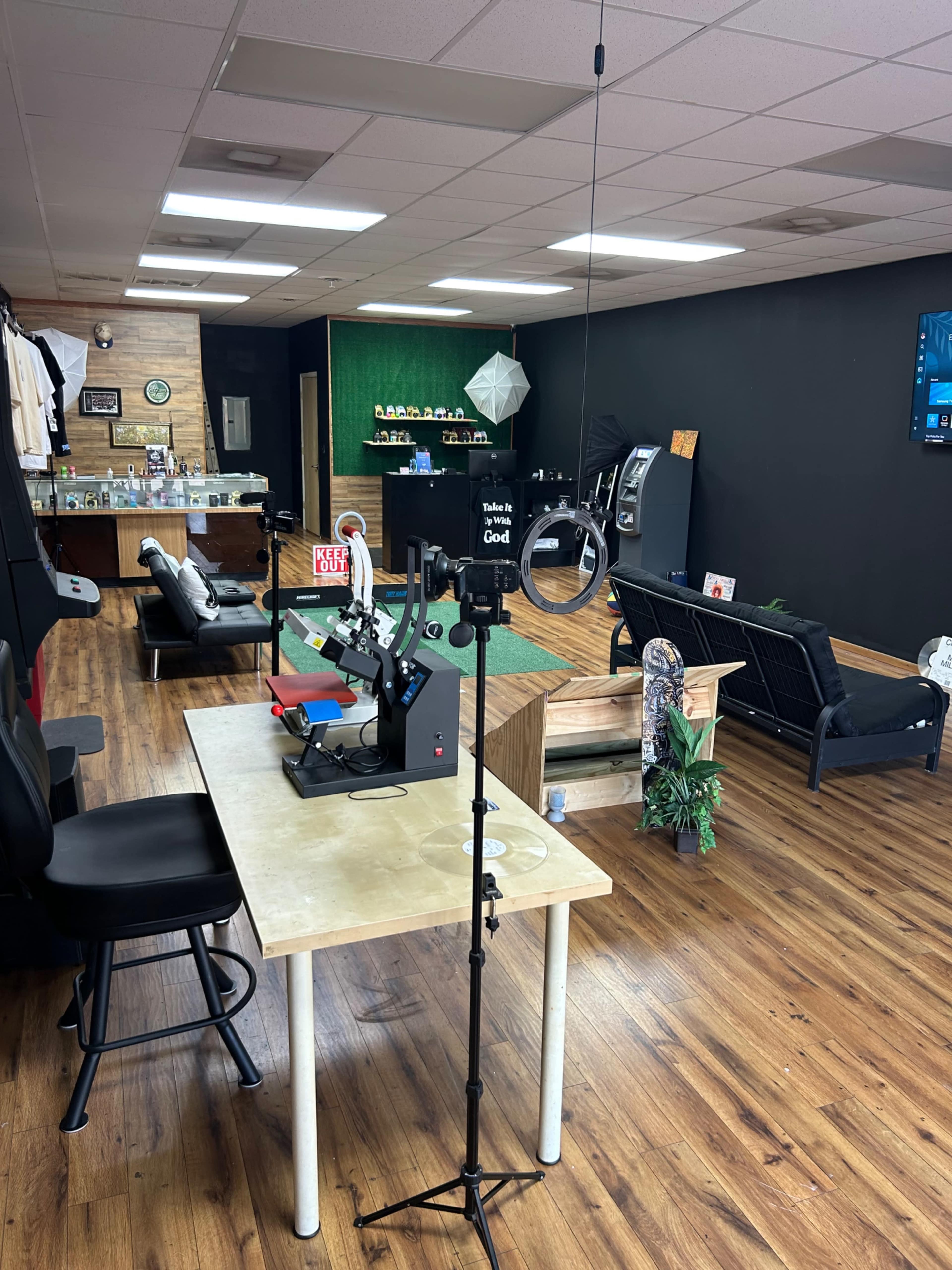 The image shows an interior of a workspace with a table featuring equipment, a ring light on a stand, and various seating areas in a well-lit room.