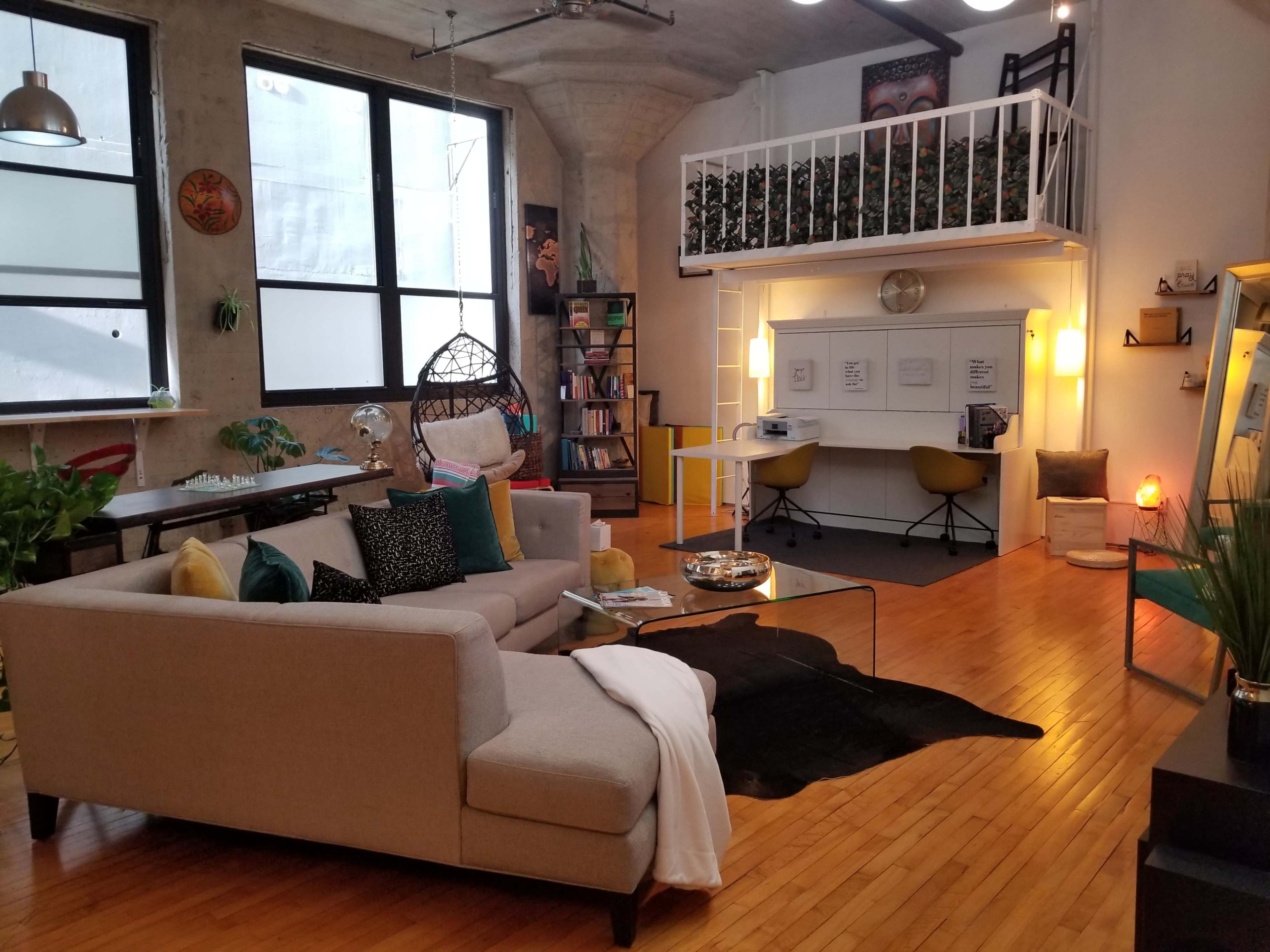 A modern open-concept living space with a sofa, a glass coffee table, a lofted bed area, and a workspace featuring two chairs and a round table.
