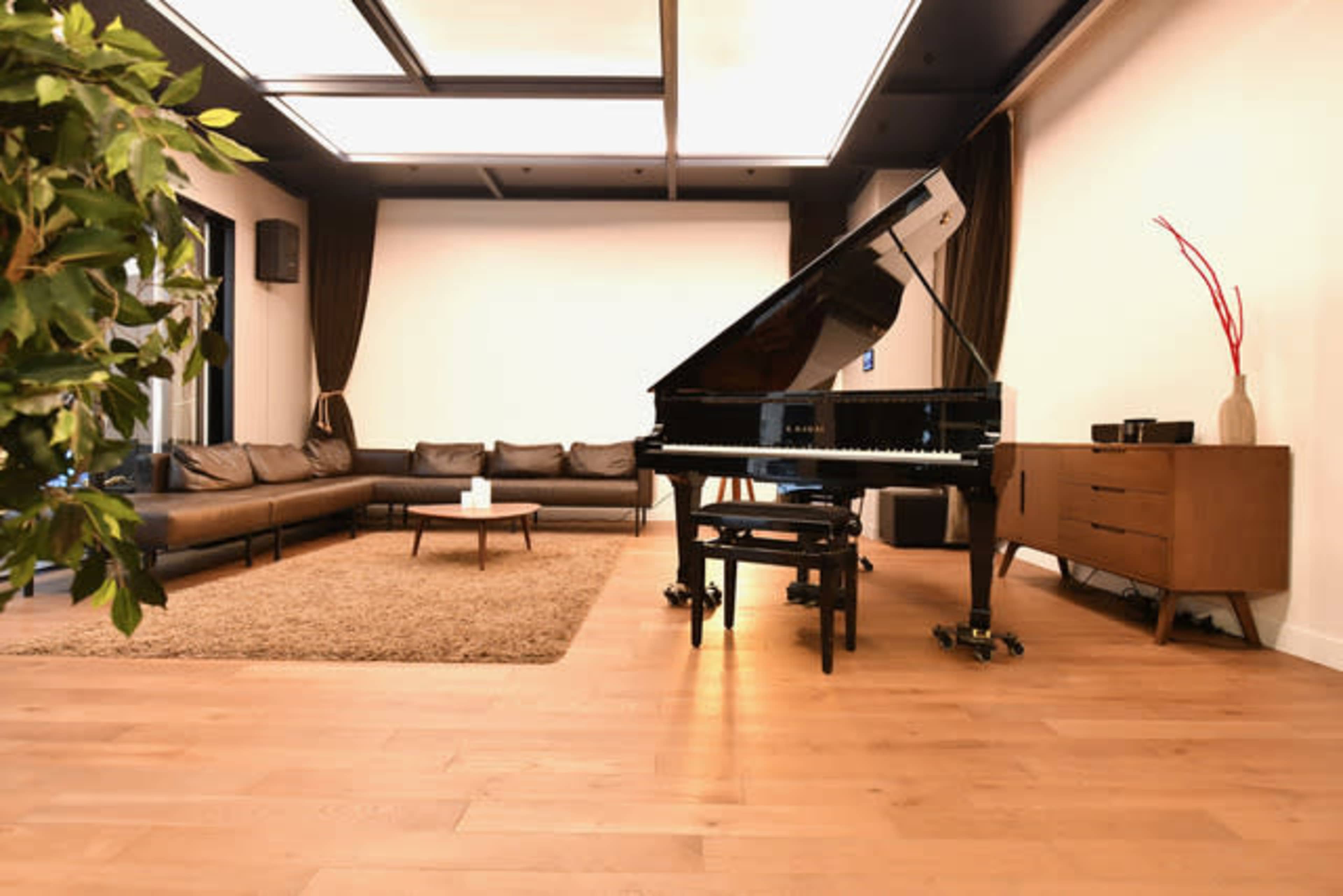 A grand piano sits beside a modern sofa in a spacious, well-lit living area with wooden flooring and minimalist decor.