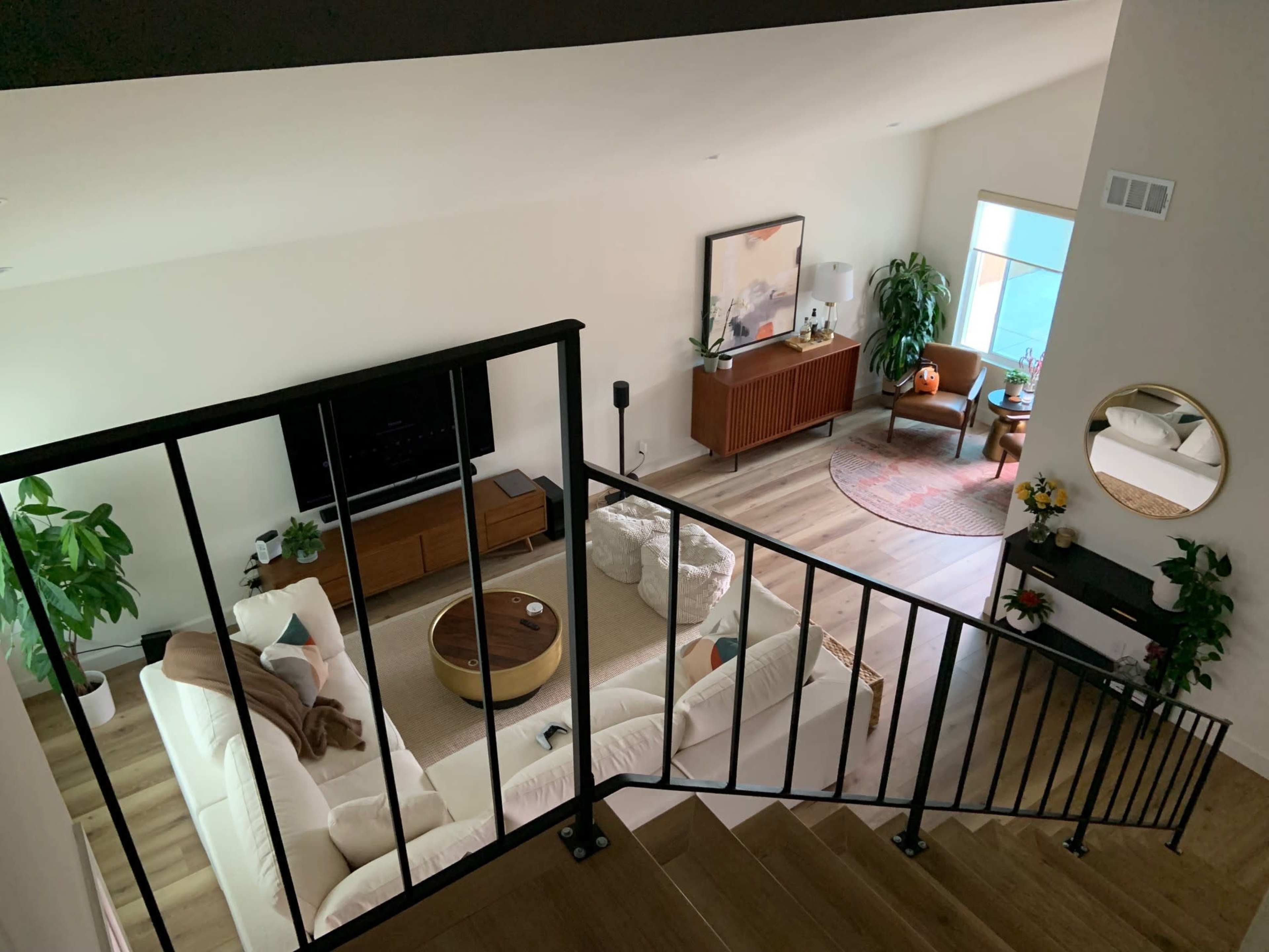 A bright living room with a large white sectional sofa, a circular coffee table, and a decorative plant, viewed from an upstairs landing.