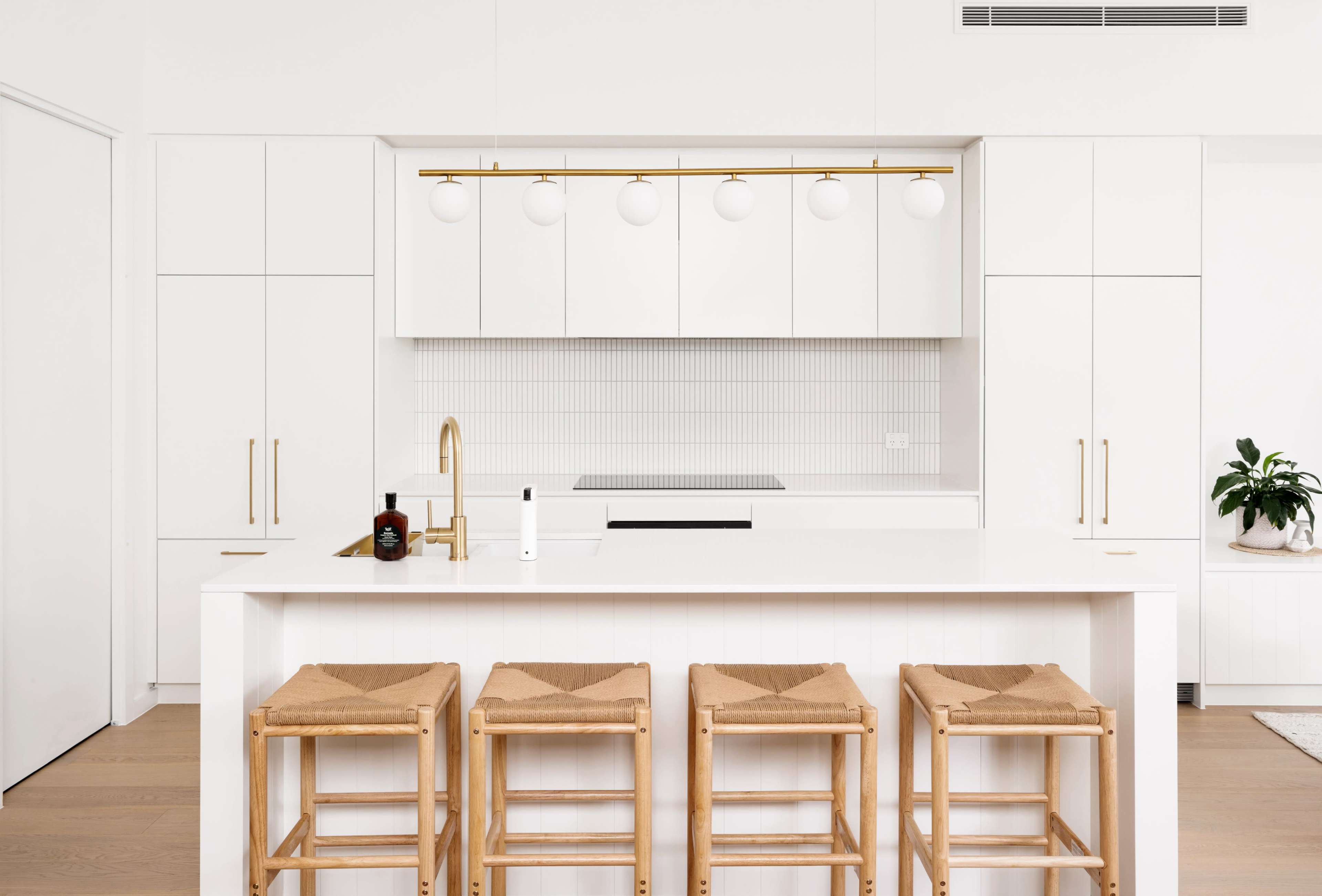 A modern kitchen features a white cabinetry design, a central island with four wooden bar stools, and pendant lighting above.