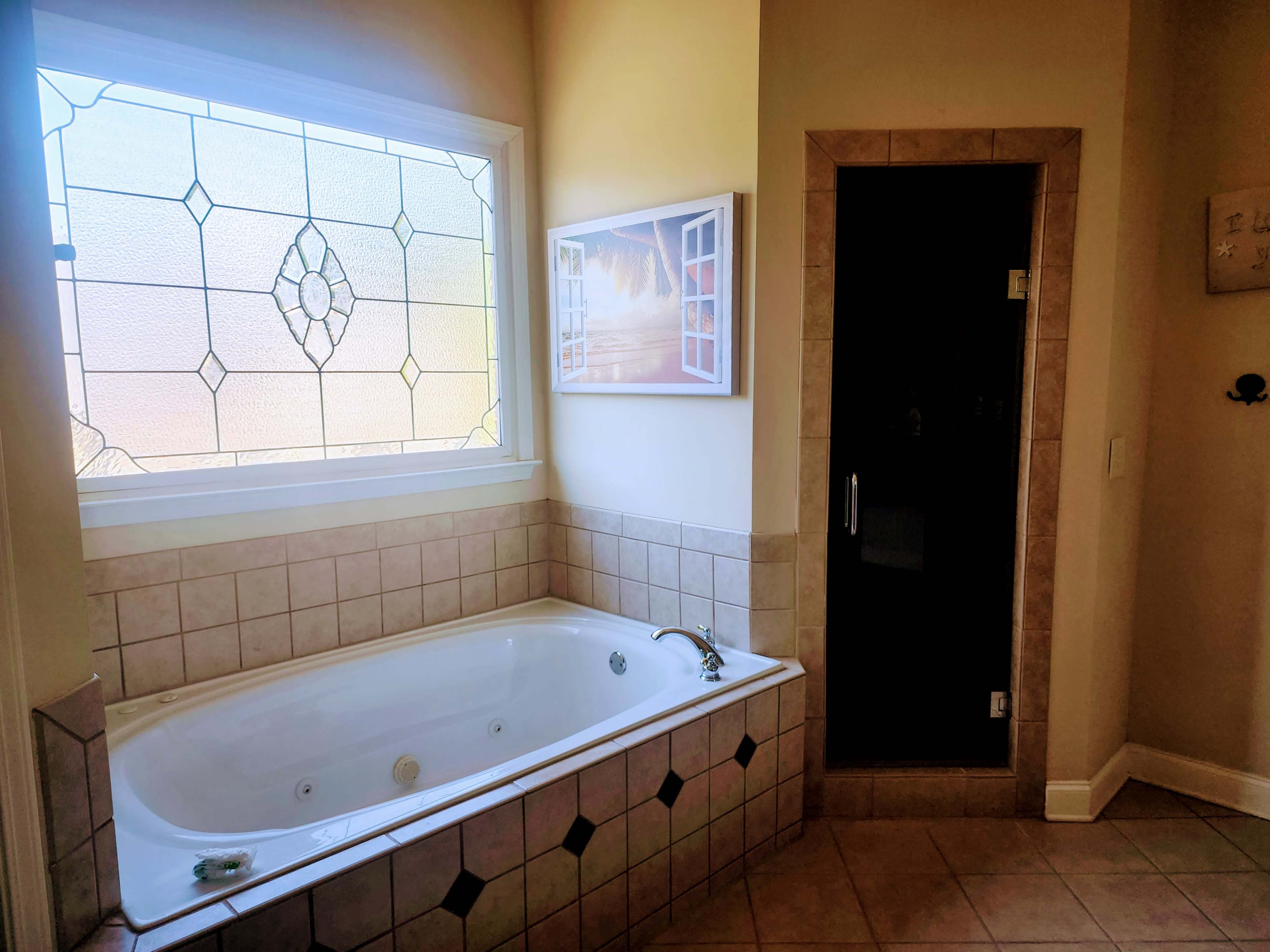 A bathroom featuring a white jetted bathtub next to a glass-enclosed shower and a decorative window.