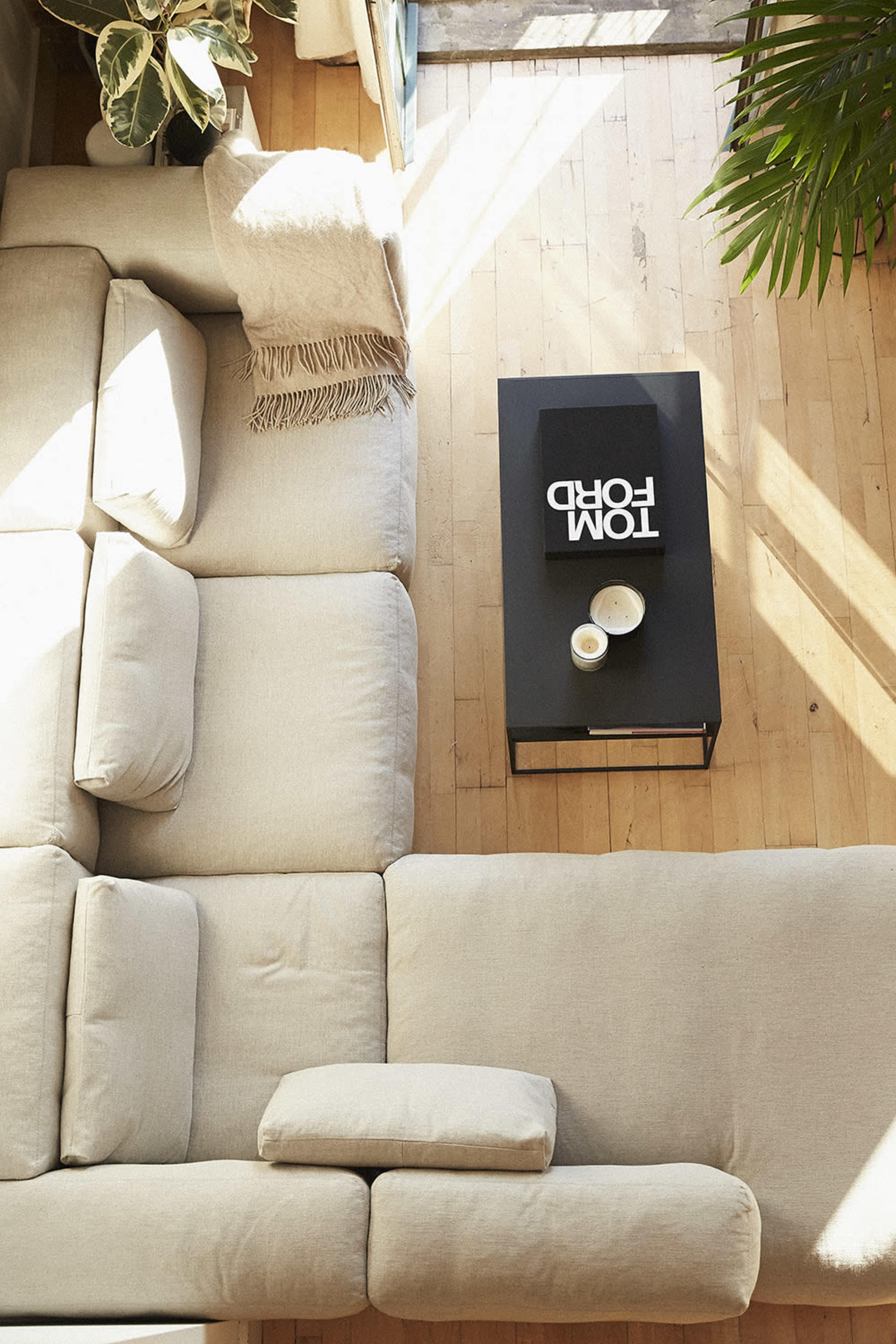 A light-colored sectional sofa is positioned on a wooden floor, with a black coffee table in the center displaying a book and a bowl.