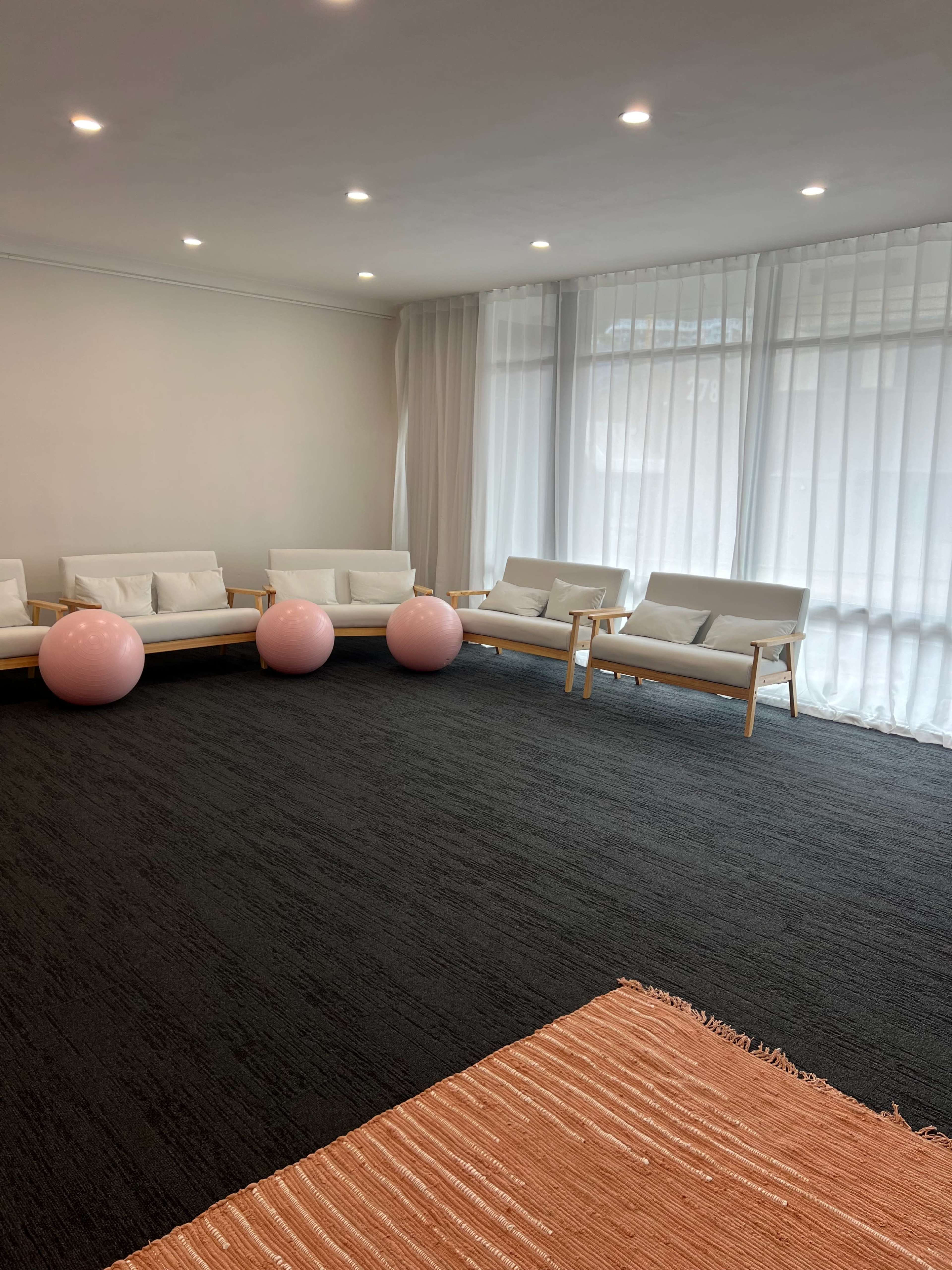 The image shows a minimalistic room with white sofas, two pink balls, large windows, and a dark carpet.