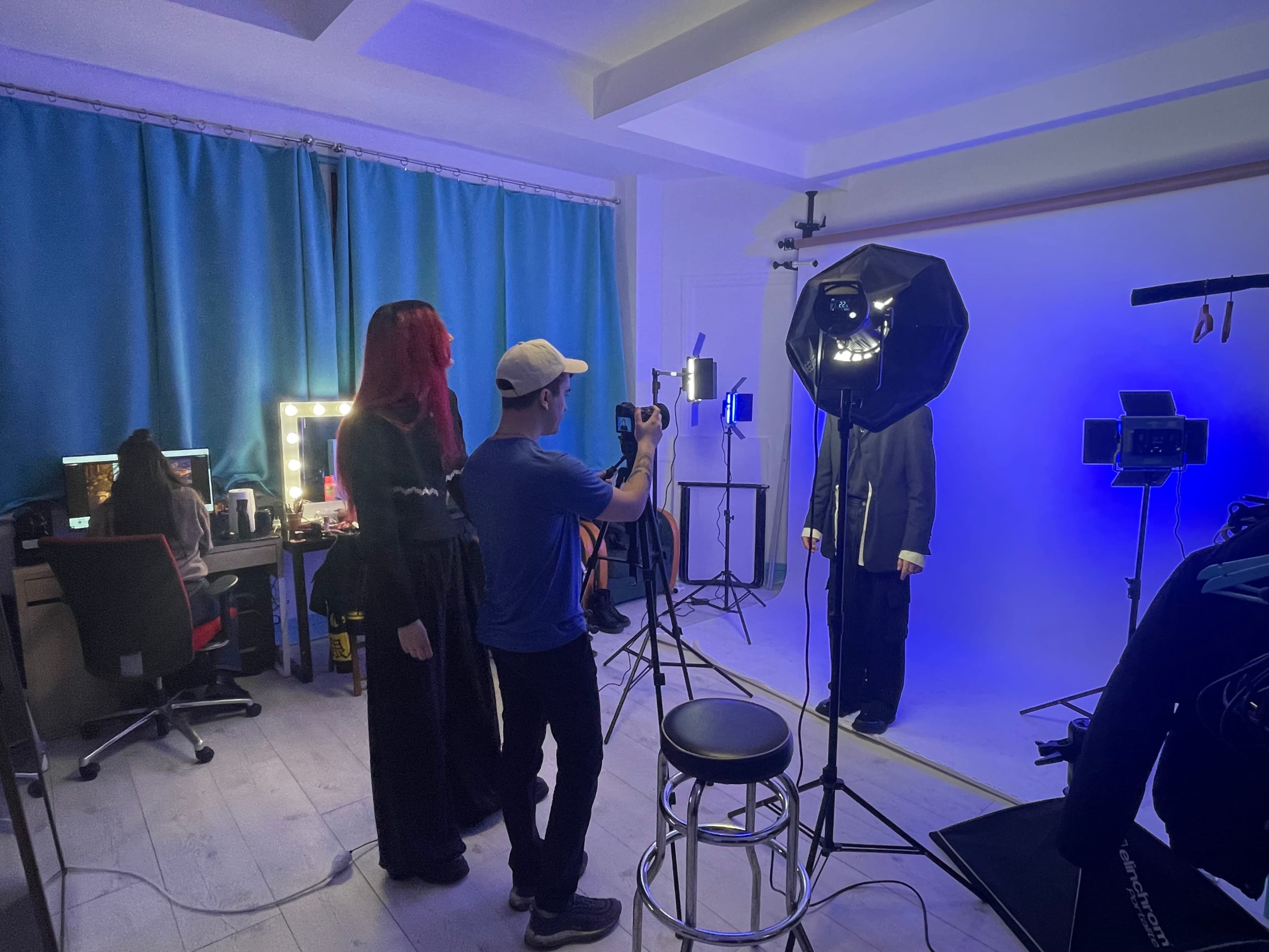 A photographer captures an individual posing against a blue backdrop in a studio while others work at computer desks.