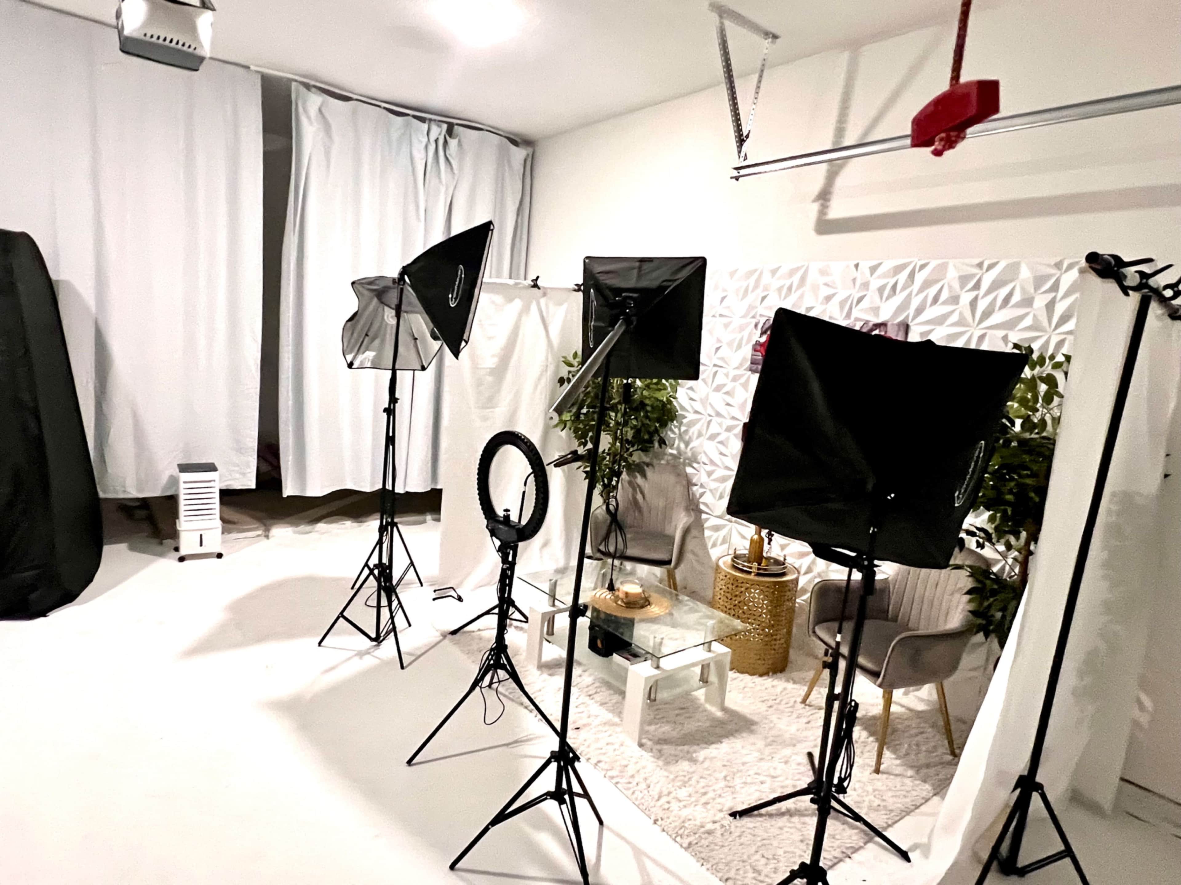 A photography studio setup features softbox lights, a ring light, and a decorative background with plants and a coffee table.