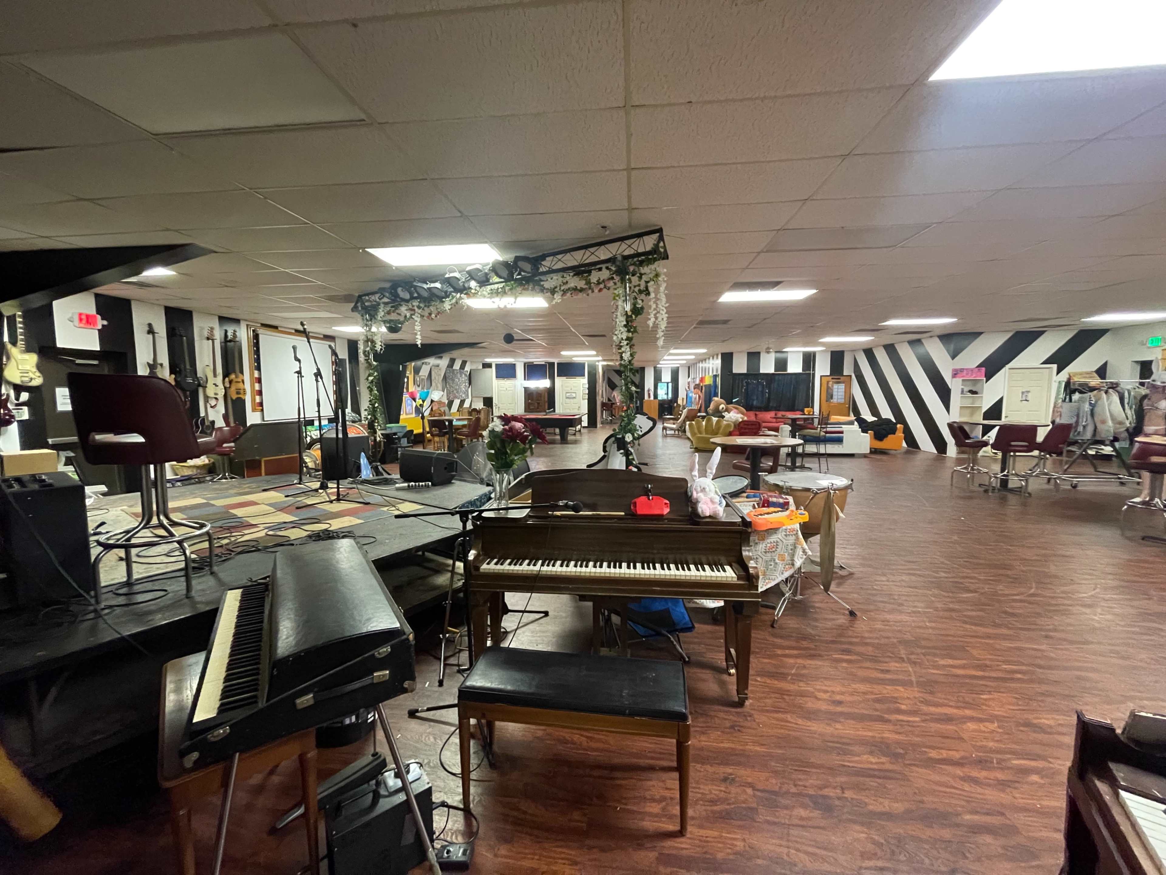 A spacious indoor venue with a stage set up for performances, featuring a piano and various seating arrangements.