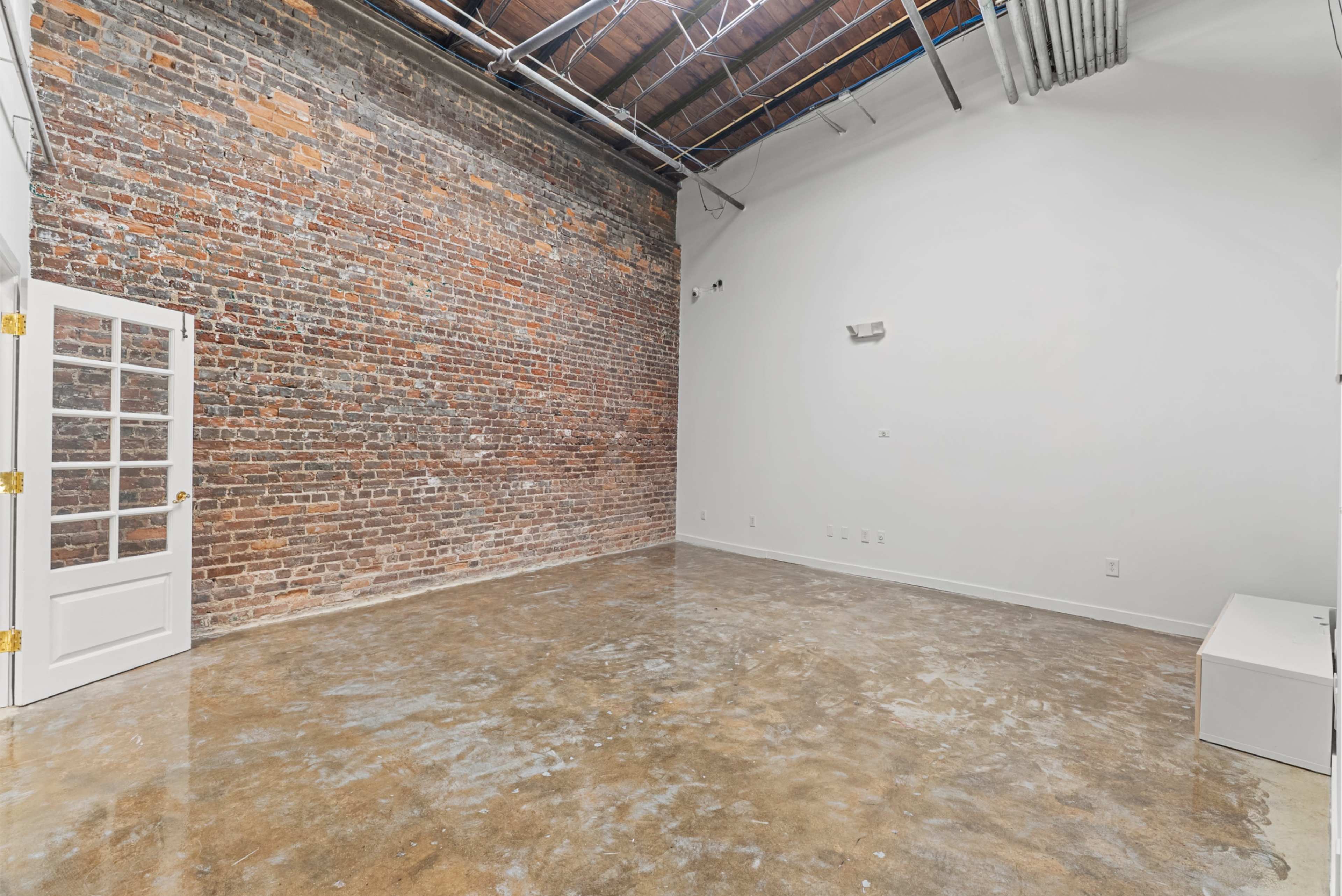 The image shows a spacious interior room with exposed brick walls and a polished concrete floor.