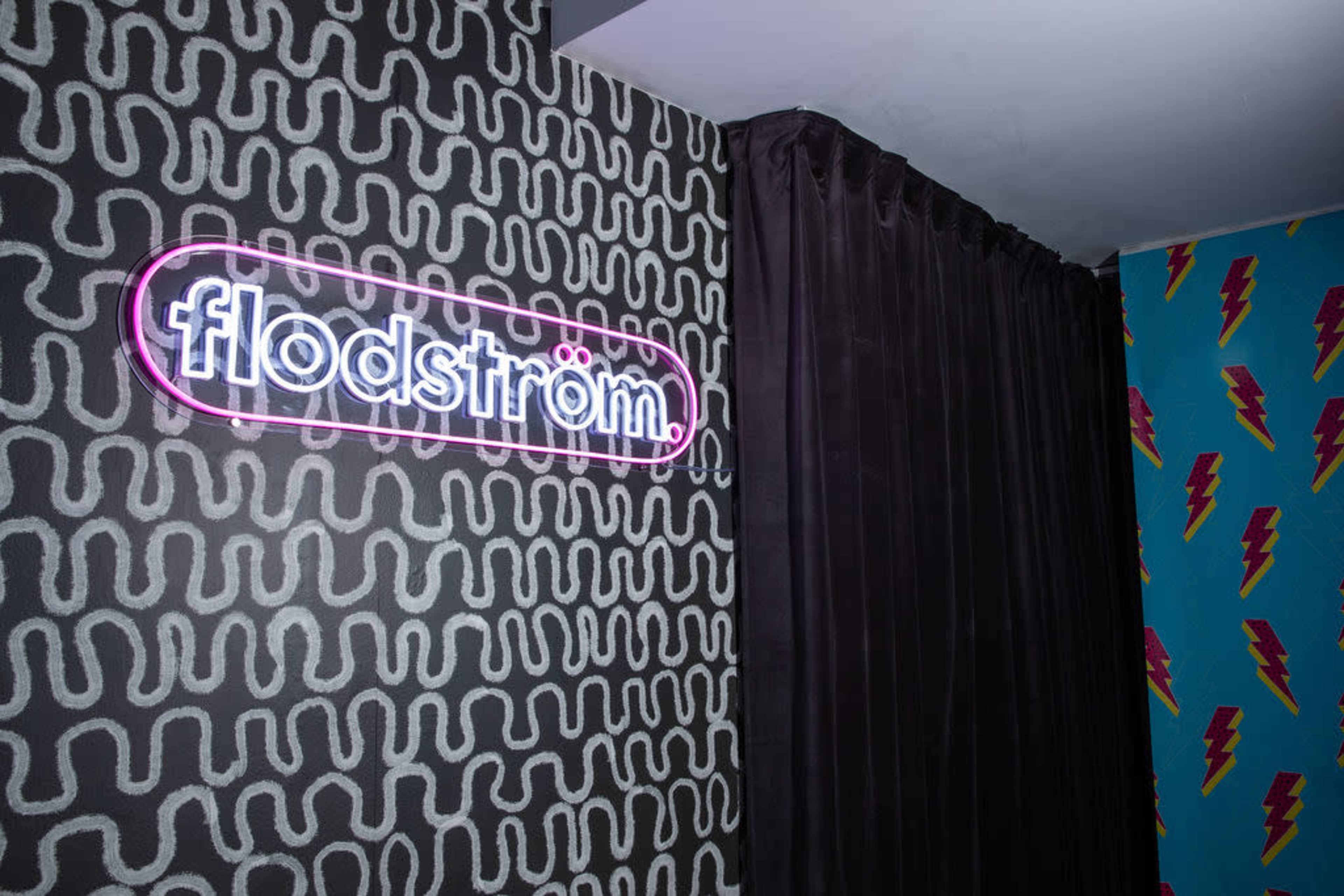 The image shows a wall with a neon sign that reads "flodström" alongside a patterned wall featuring colorful lightning bolts.