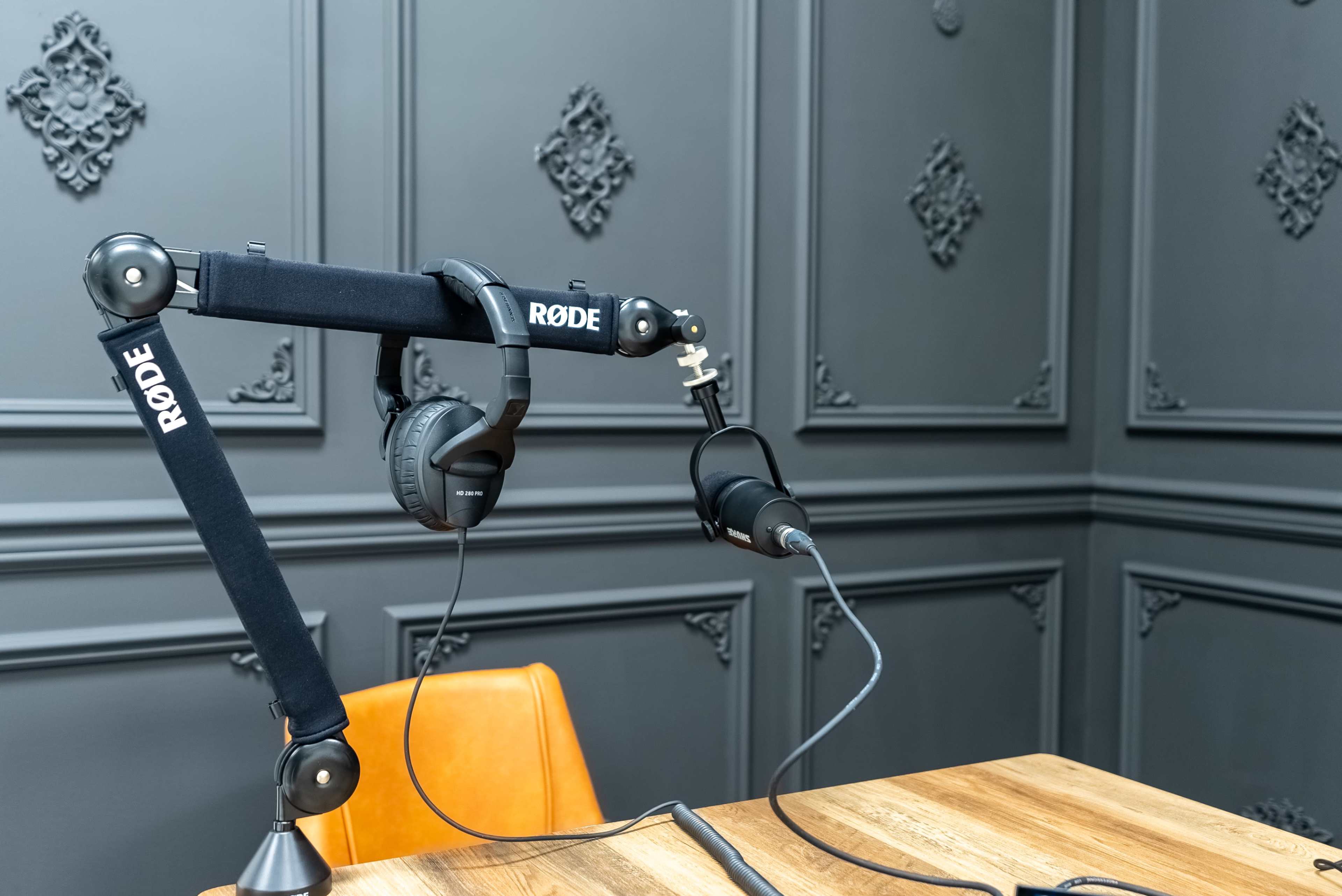 A microphone and headphones are mounted on a Rode boom arm in a room with dark, textured walls.