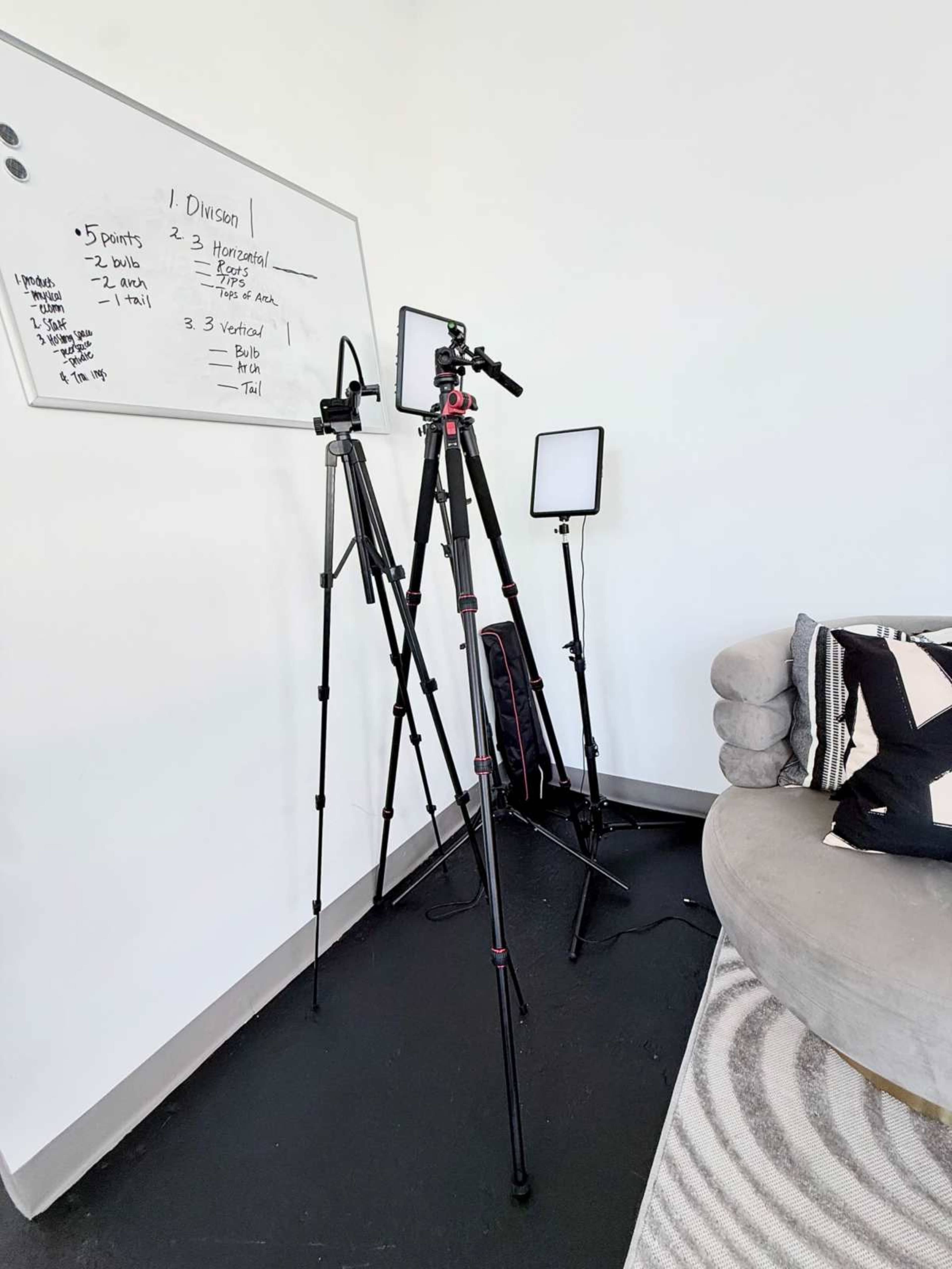 The image shows a corner of a room featuring three tripods with lighting and a whiteboard with handwritten notes.