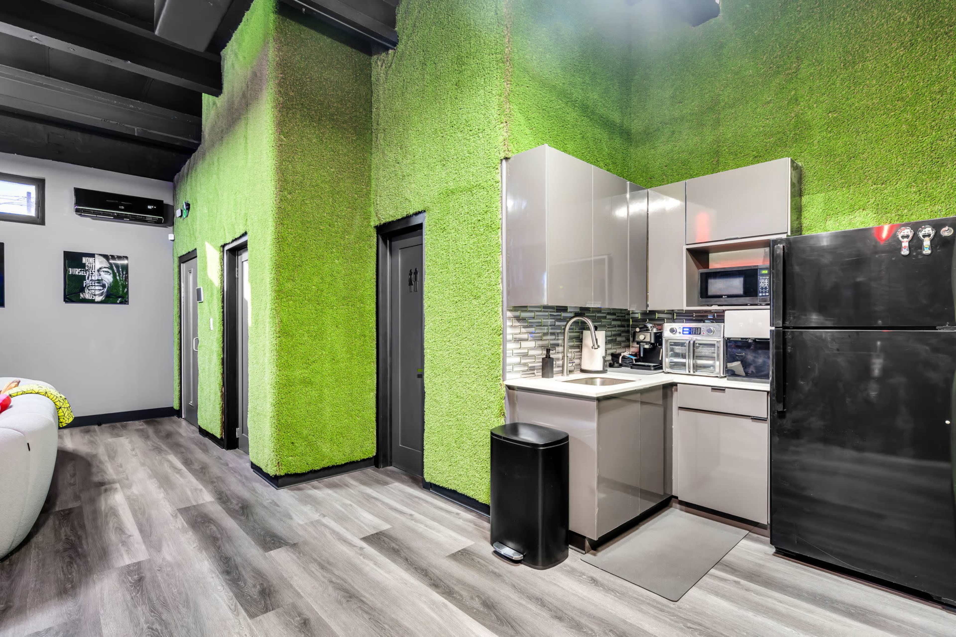 The image shows a modern kitchen with green, textured walls, sleek gray cabinets, and black appliances.