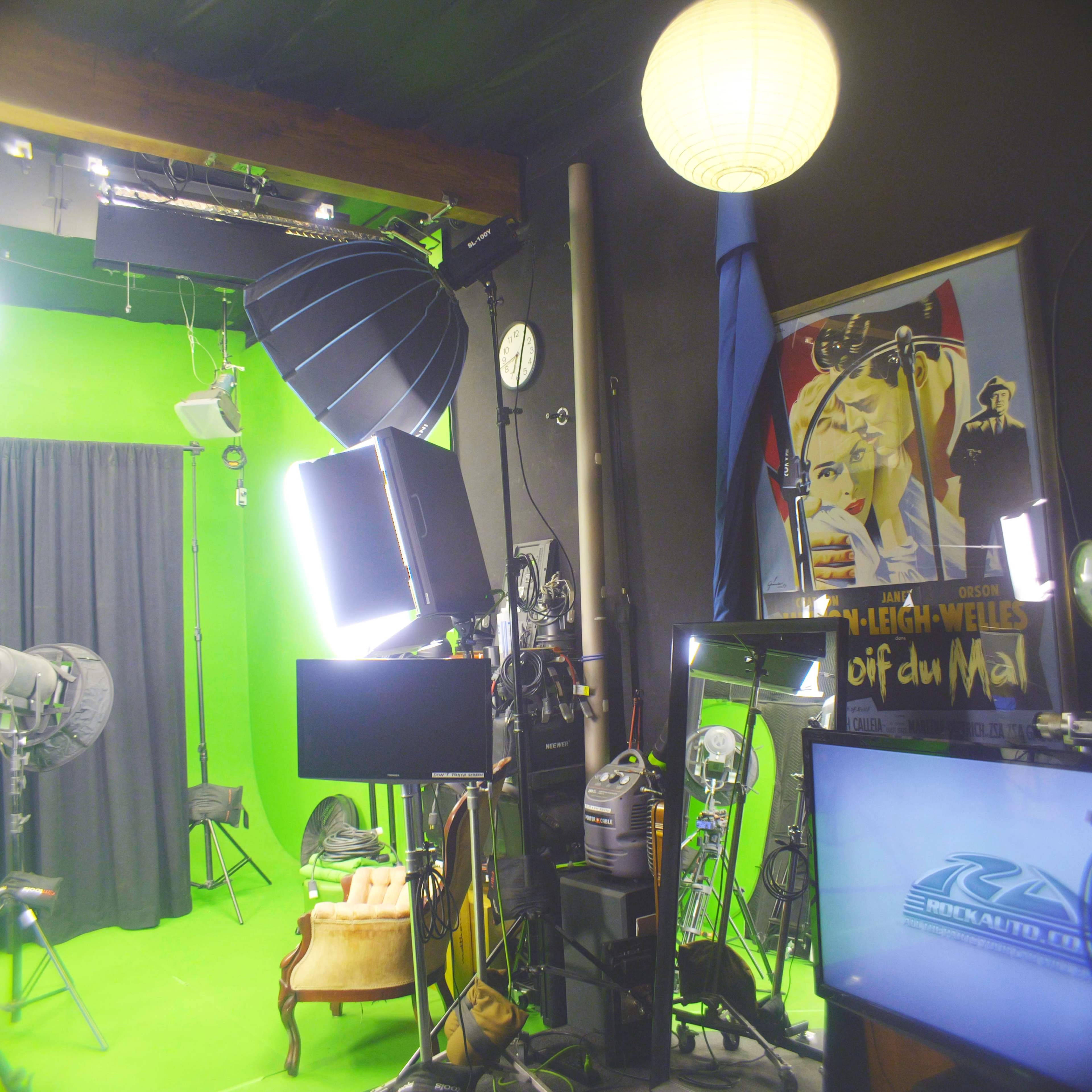 The image shows a studio with a green screen backdrop, various lighting equipment, and a vintage poster on the wall.