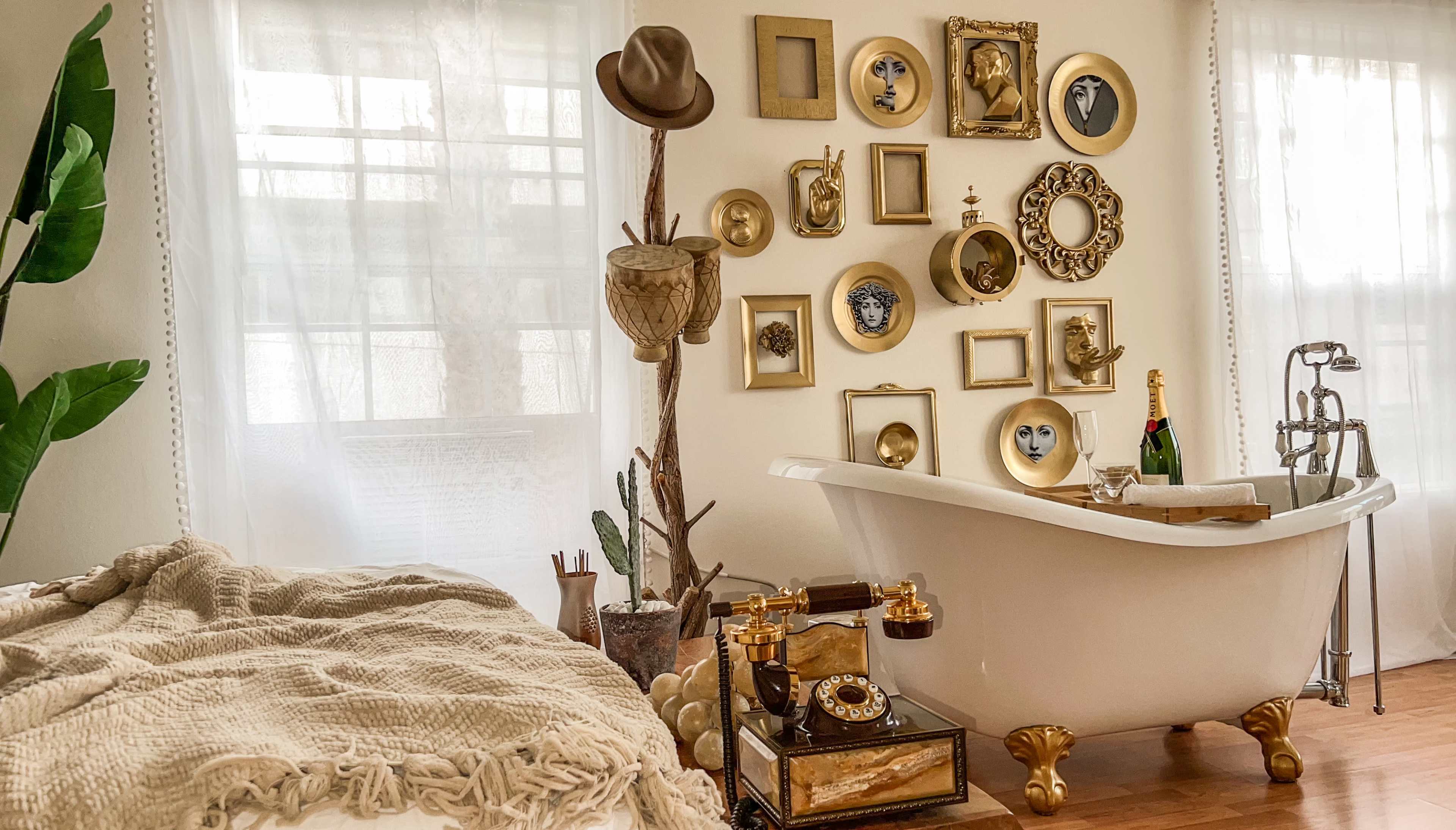 A vintage-style bathroom featuring a freestanding bathtub, decorative wall art in gold frames, and a small side table with a vintage telephone and champagne.