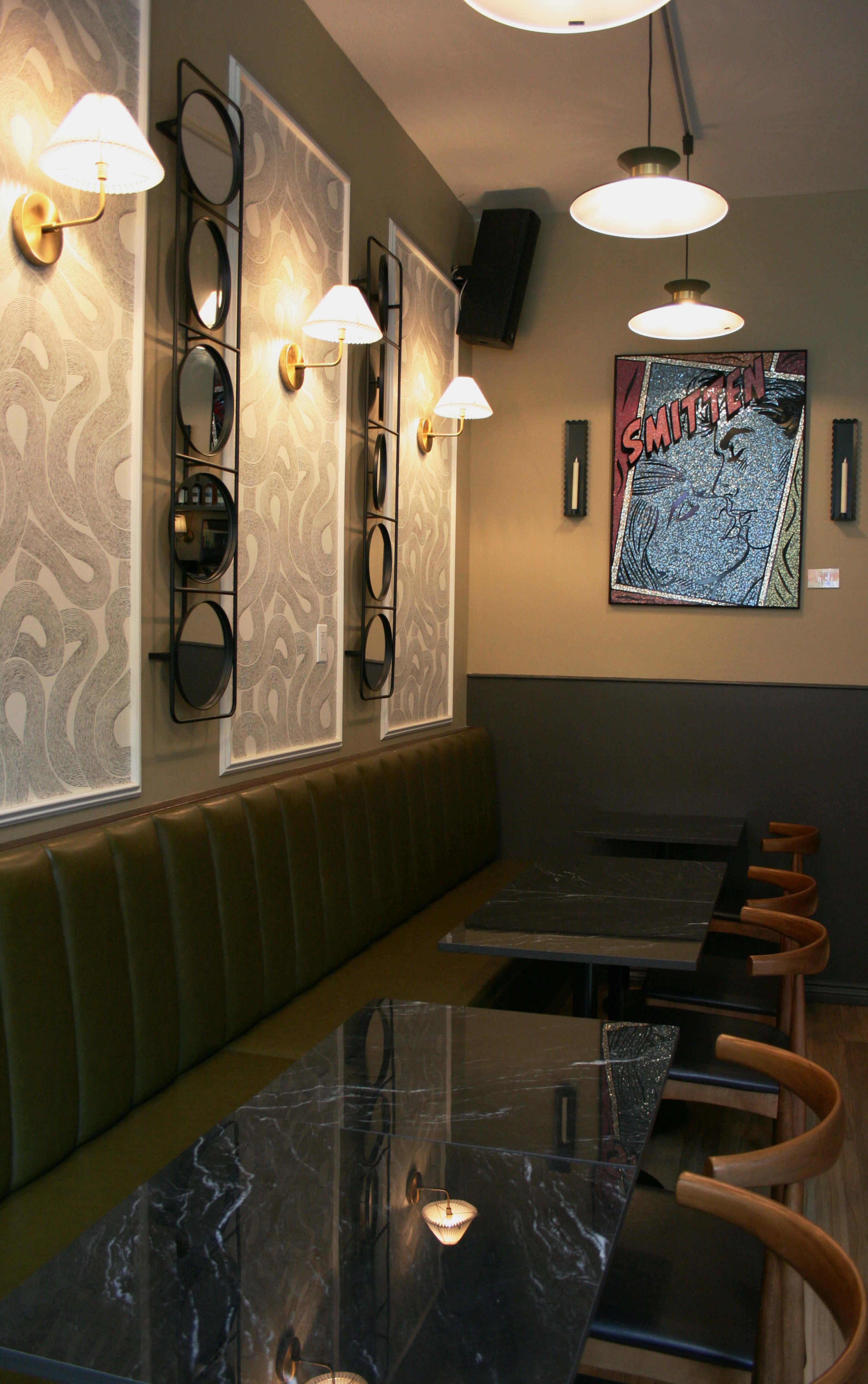 The image shows a modern café interior with green upholstered seating, dark marble tables, and decorative wall art.