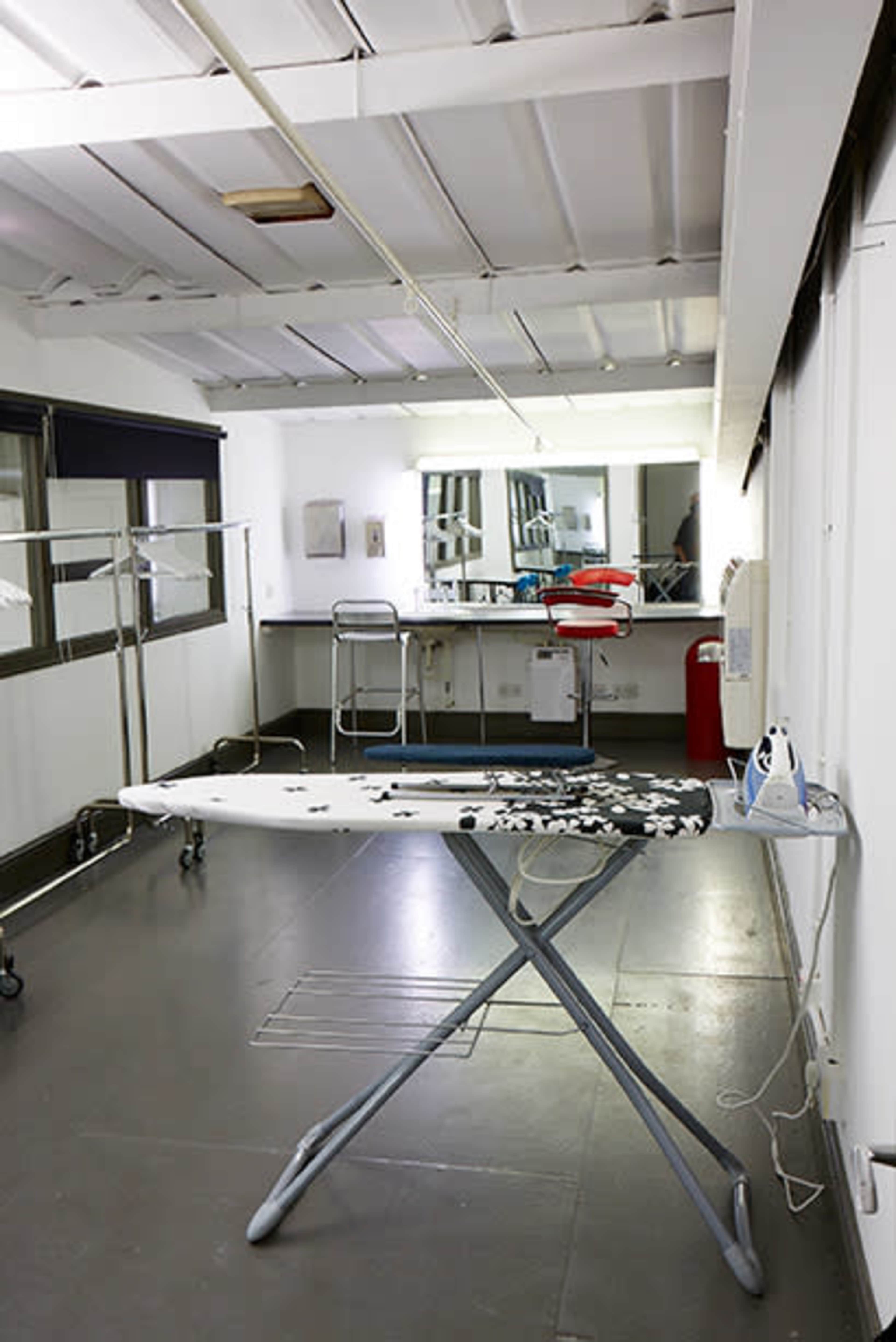 An ironing board in a sparsely furnished room featuring a mirror, a clothing rack, and an iron.