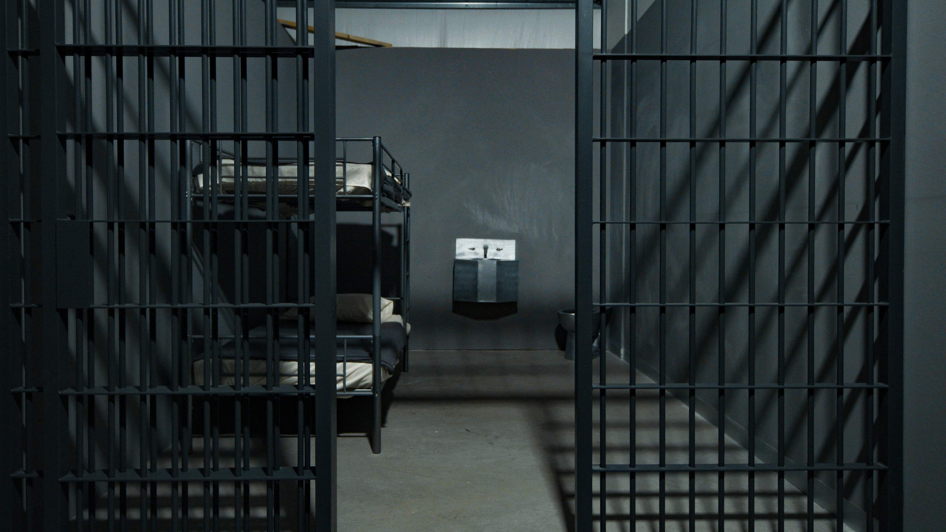 The interior of a prison cell with two metal bunk beds and a small adjoining area for a toilet and sink.