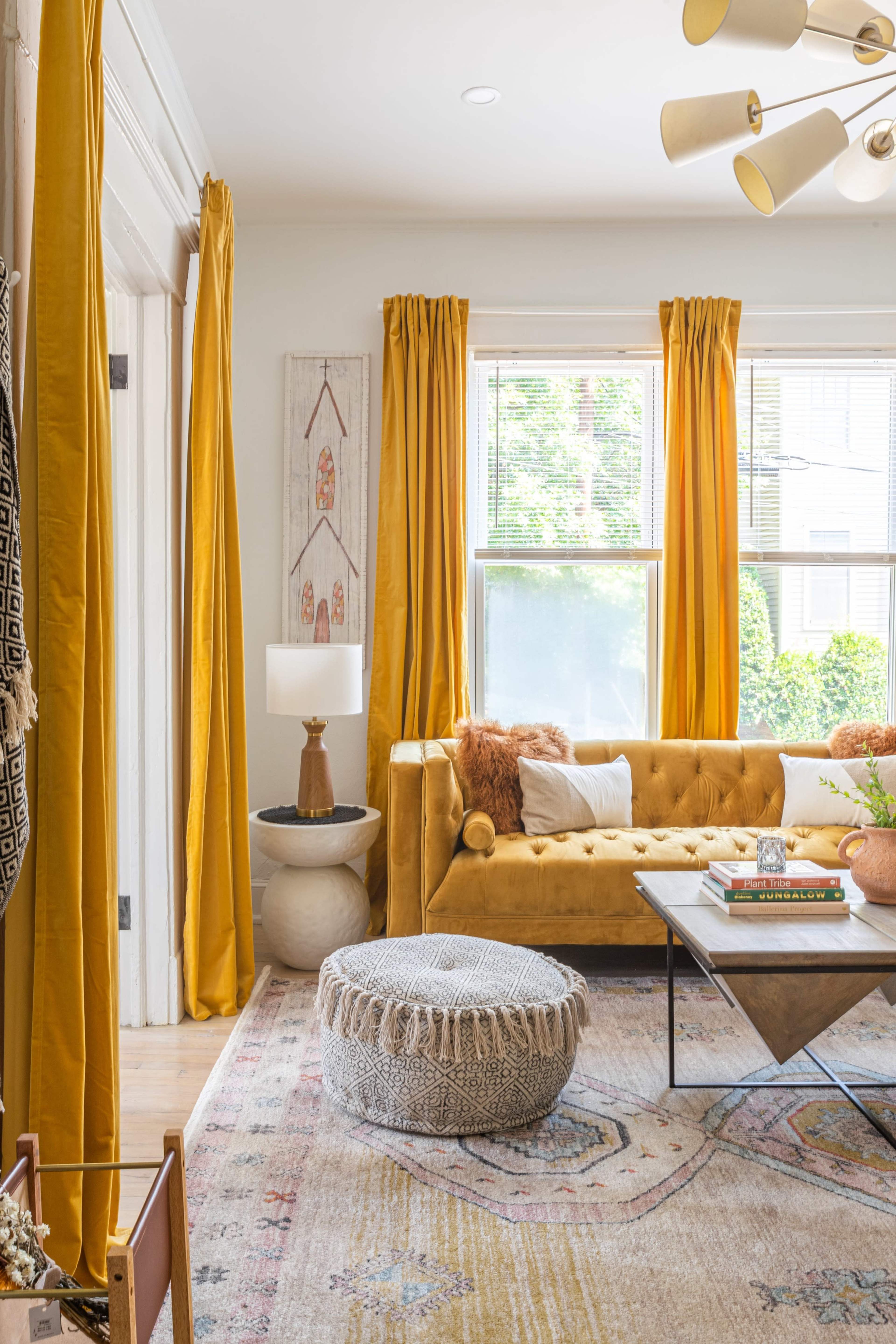 The room features a mustard-yellow sofa, coordinating curtains, a decorative coffee table, and a pouf on a patterned area rug.