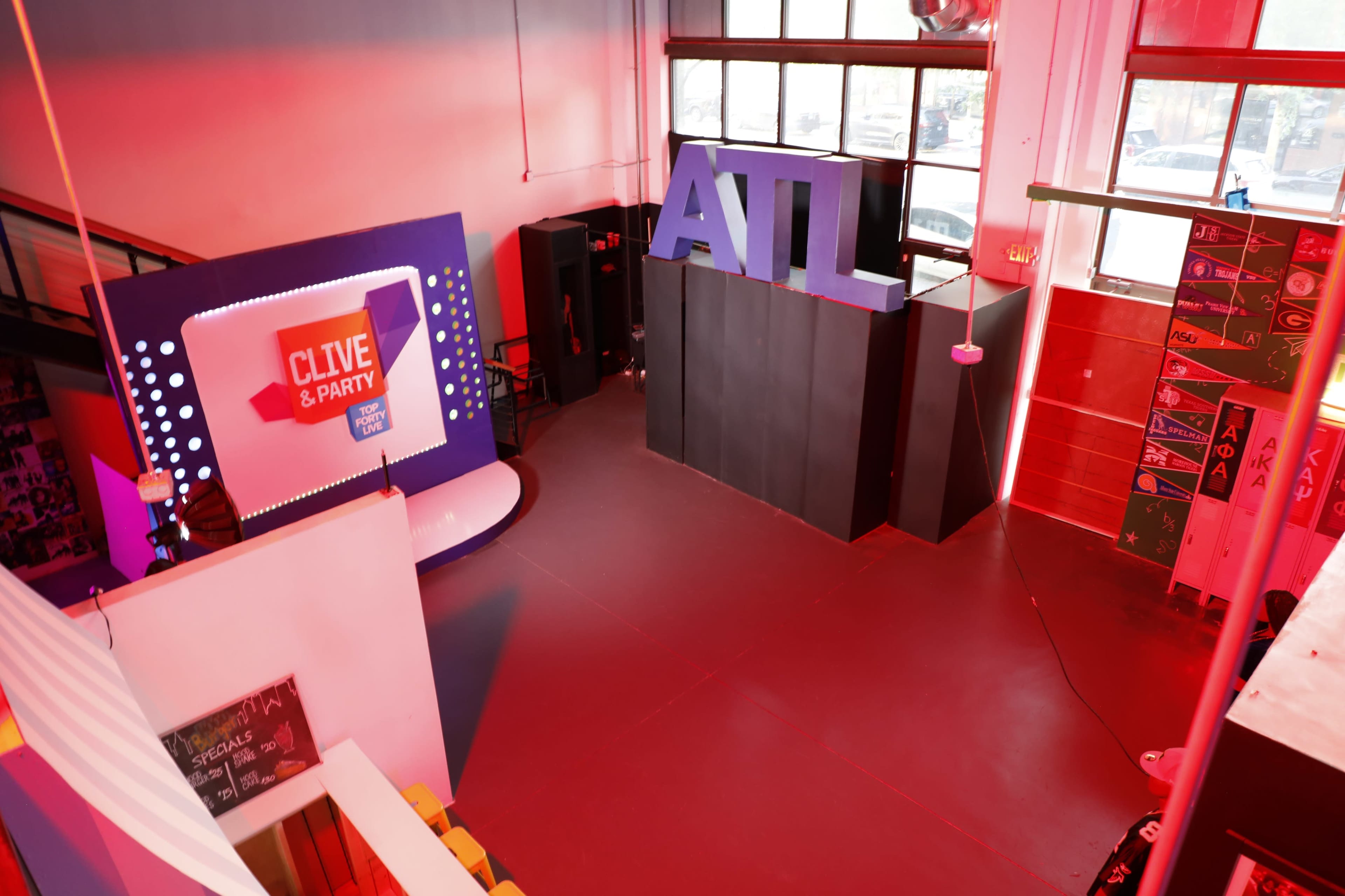 The image shows an event space with a stage featuring a "CLIVE & PARTY" sign and large "ATL" letters, illuminated by red lighting.