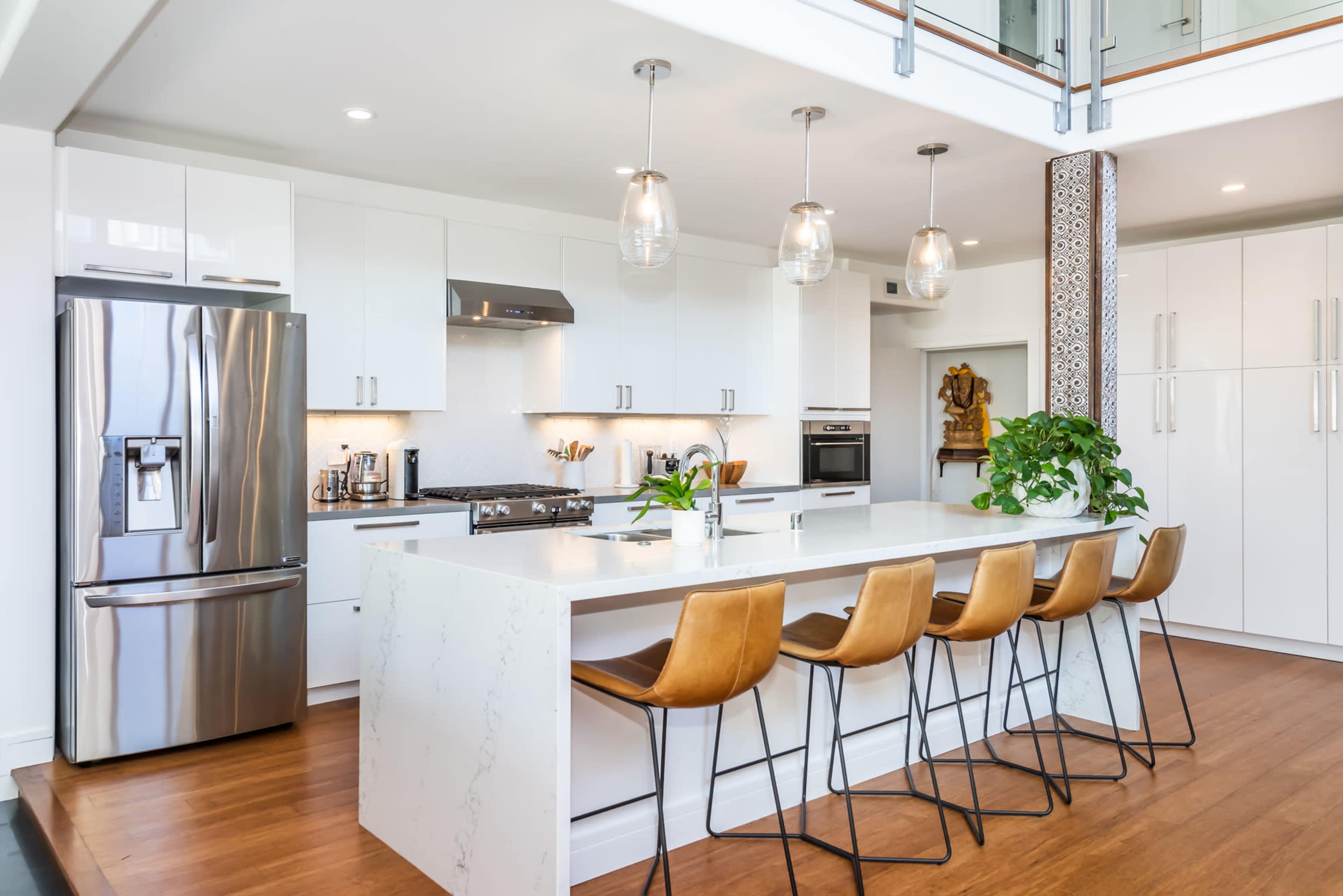 A modern kitchen with white cabinetry, a large island with bar stools, stainless steel appliances, and pendant lighting.
