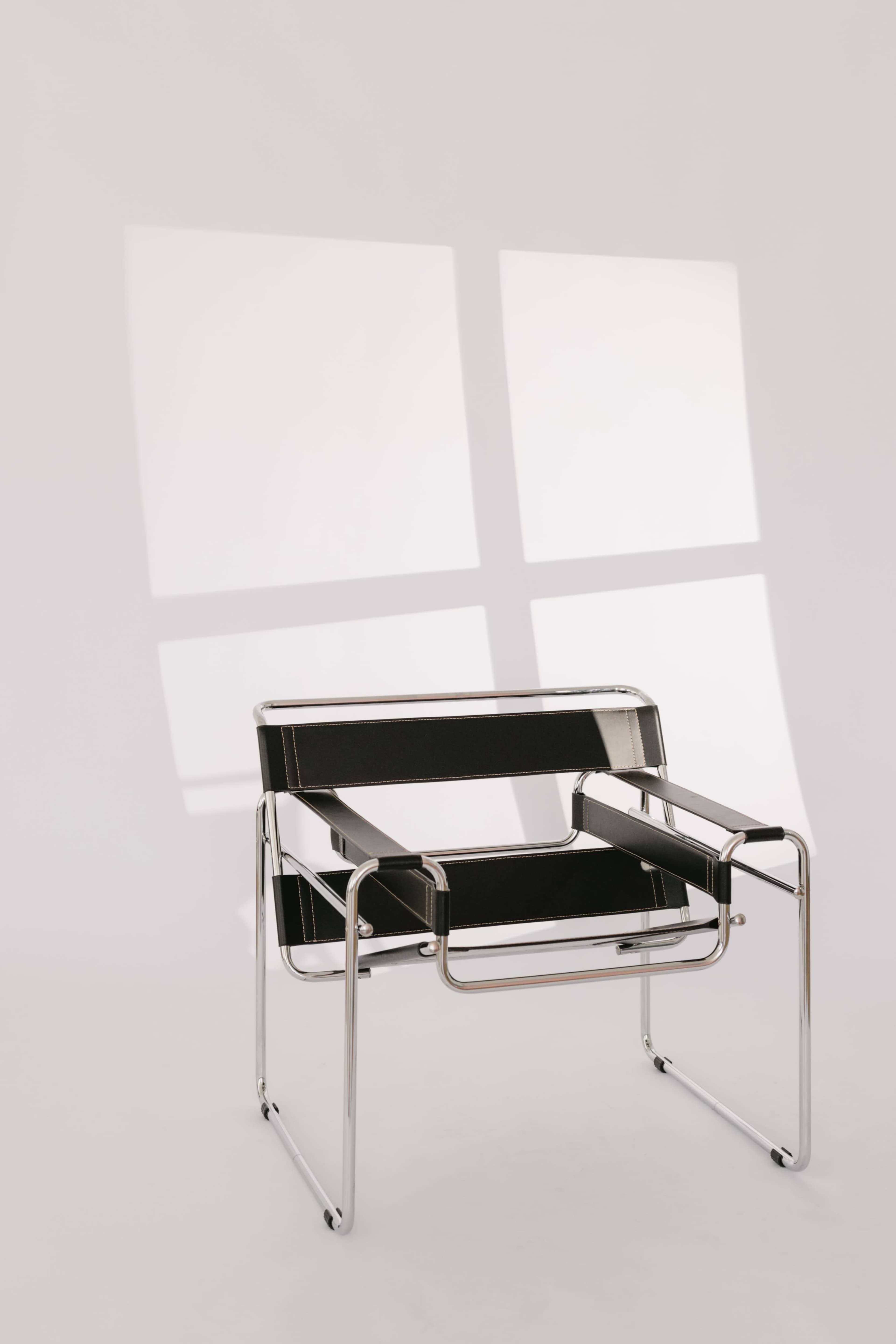 A black and chrome chair is positioned against a white wall, casting shadows that create a grid pattern.