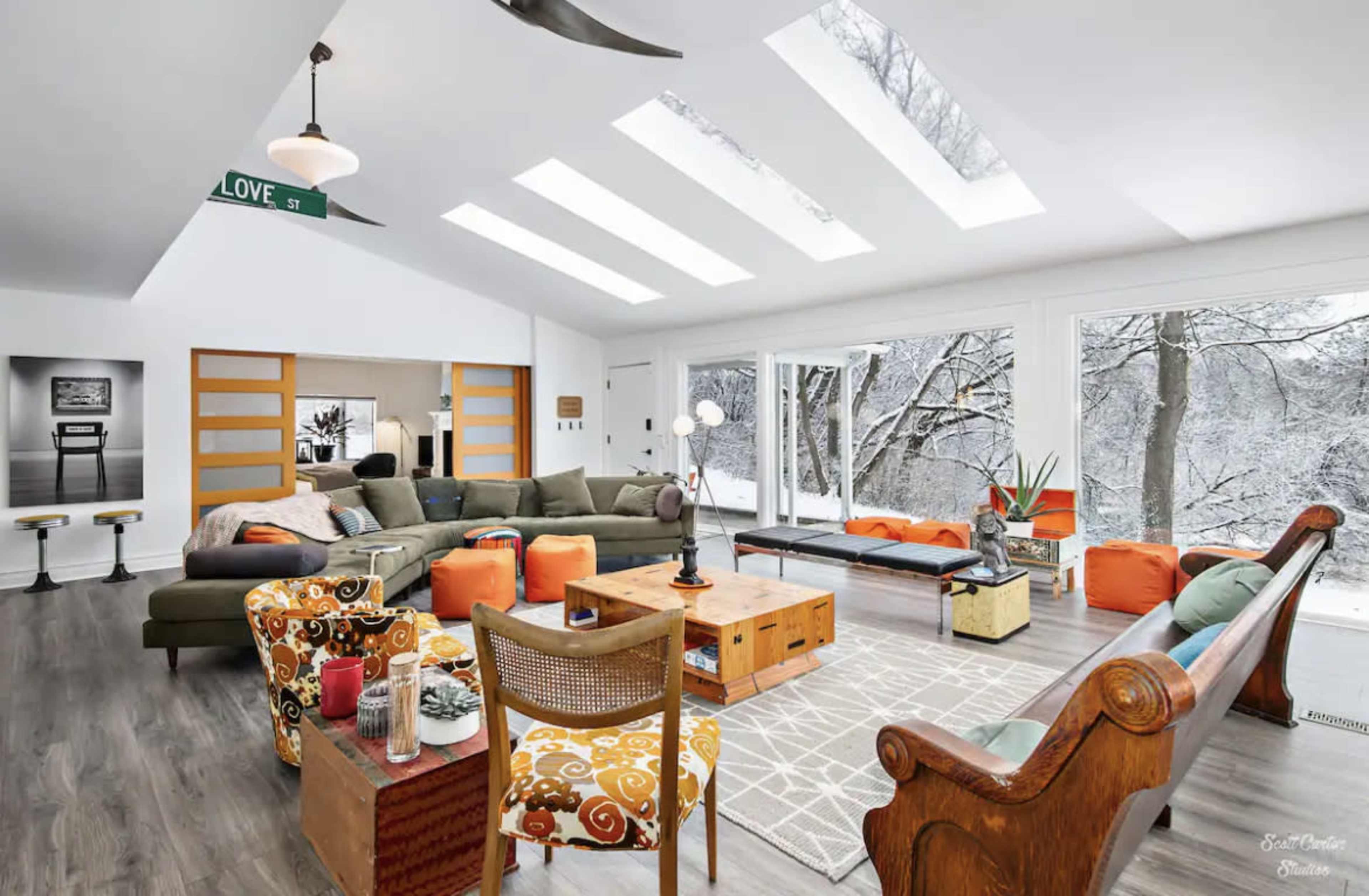 The living room features a large sectional sofa, colorful accent pillows, a wooden coffee table, and large windows that overlook a snowy landscape.