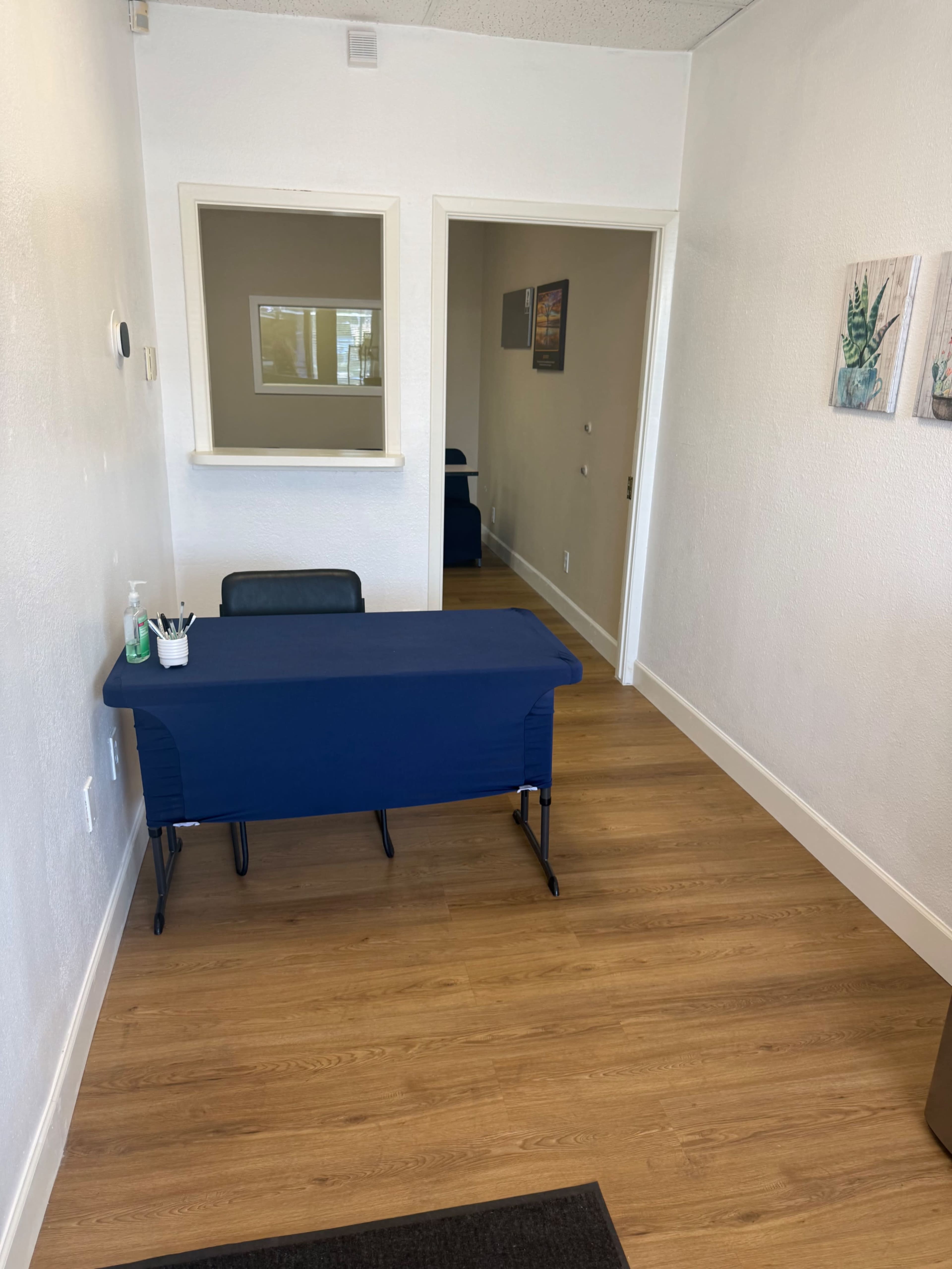The image shows a small, well-lit reception area with a navy blue table in the foreground and a doorway leading to another room in the background.
