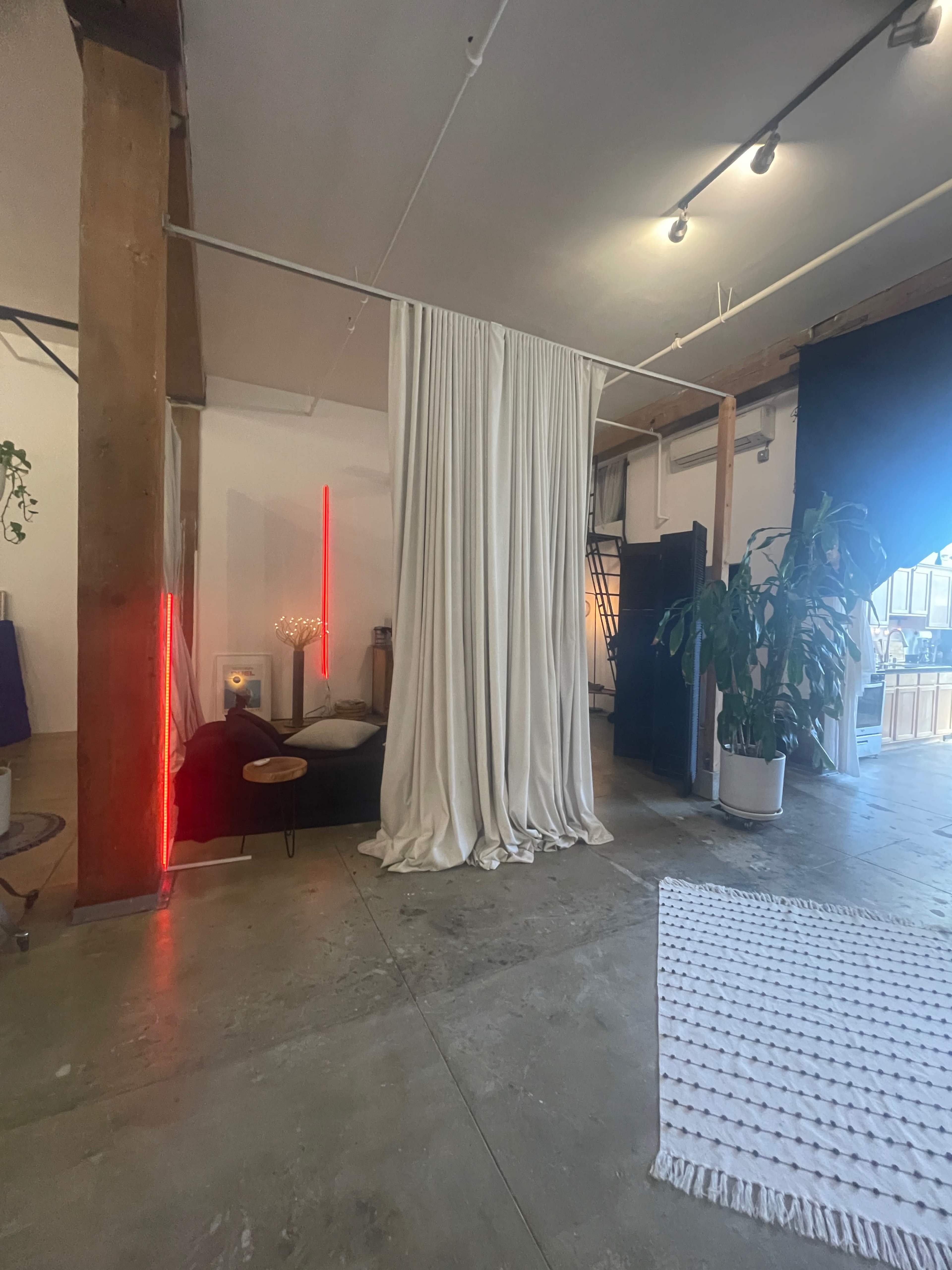 A spacious interior with a white curtain dividing the area, a sofa, a potted plant, and ambient lighting primarily from red neon strips.