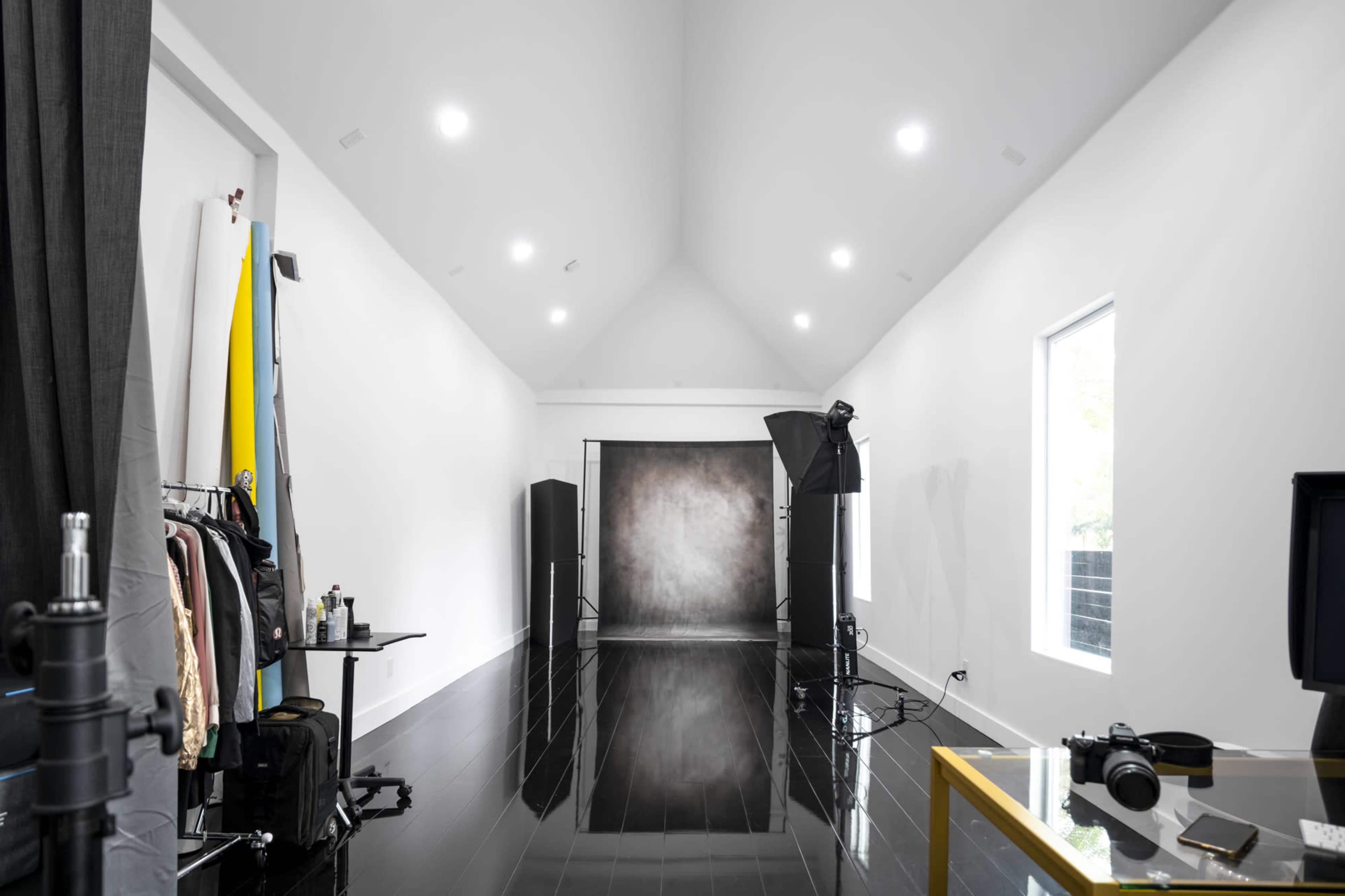 A spacious photography studio with a reflective black floor, a seamless backdrop, and various photography equipment arranged along the sides.