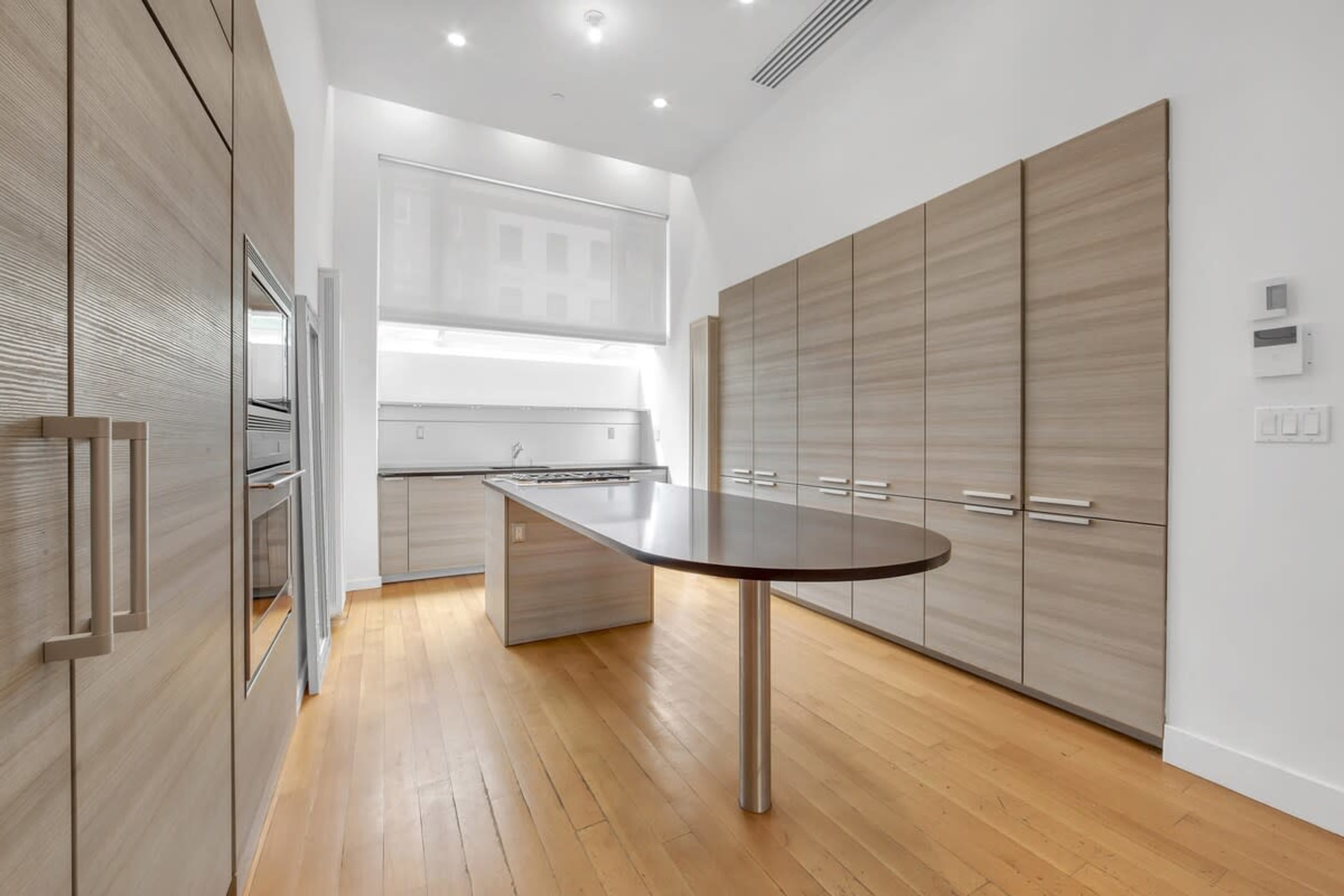The image shows a modern kitchen with sleek cabinetry, a central island, and wooden flooring.