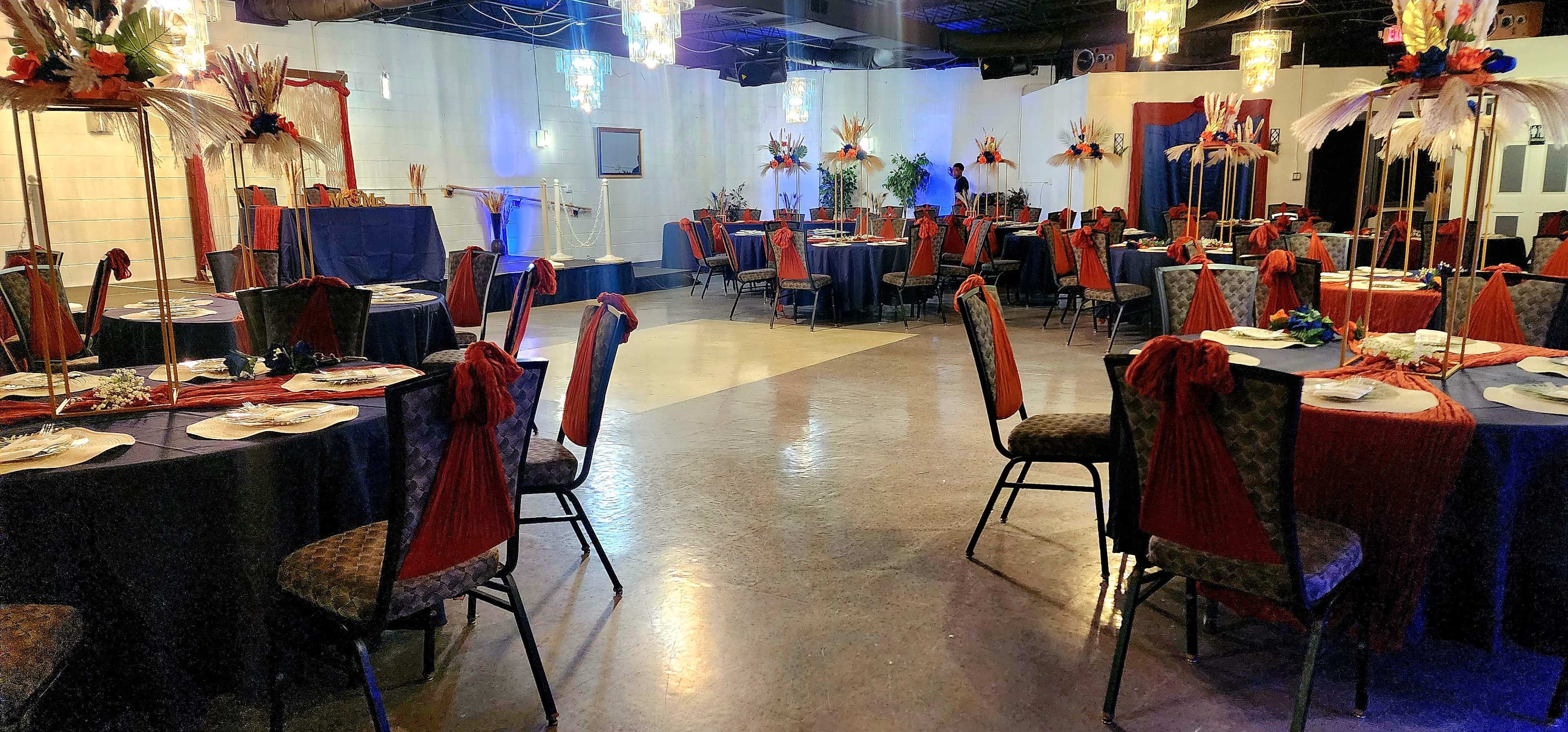 The image shows a banquet hall set up for an event, featuring round tables adorned with centerpieces and decorated chairs.