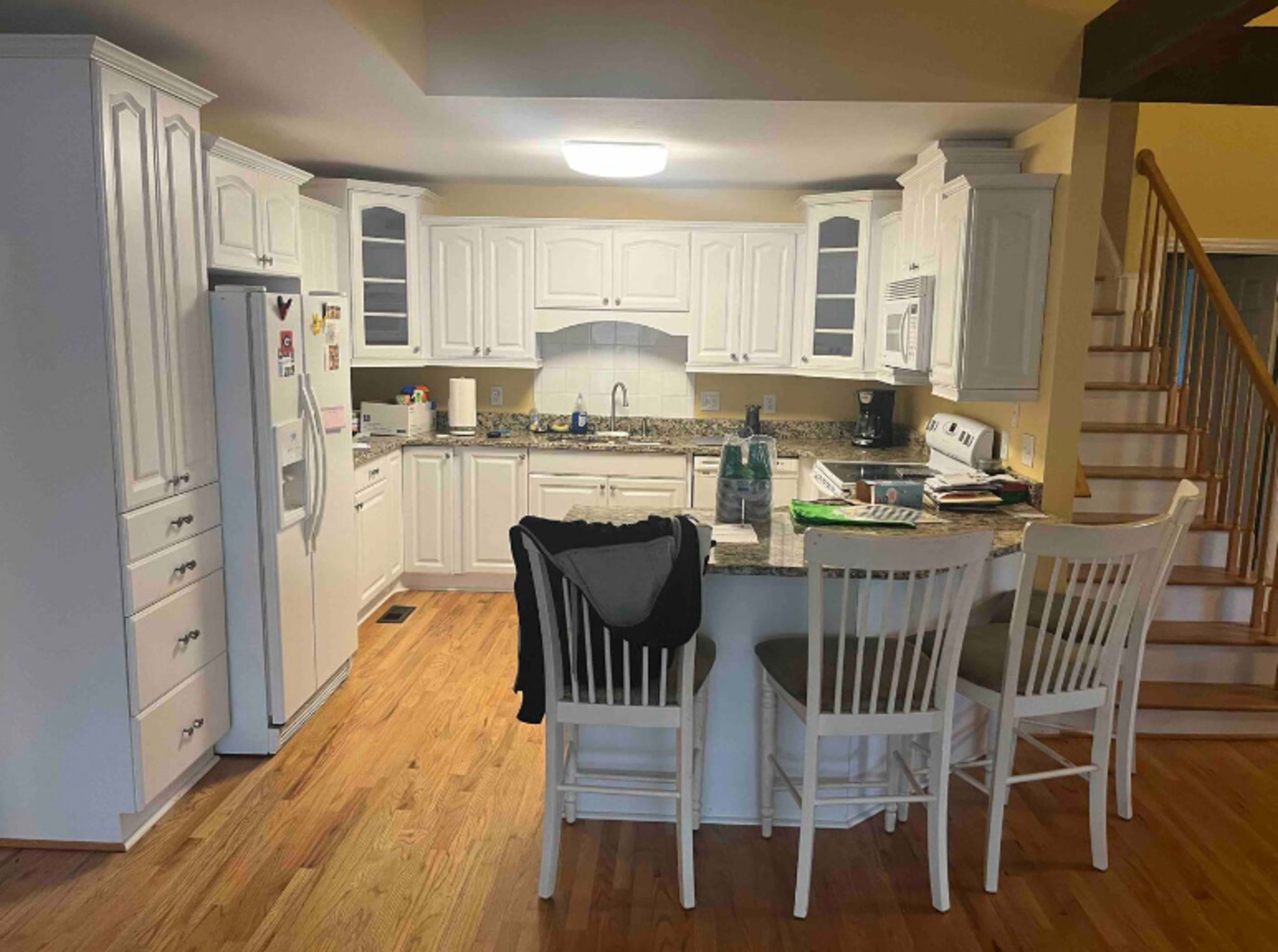 The image shows a modern kitchen with white cabinets, a central island with seating, and wooden flooring.