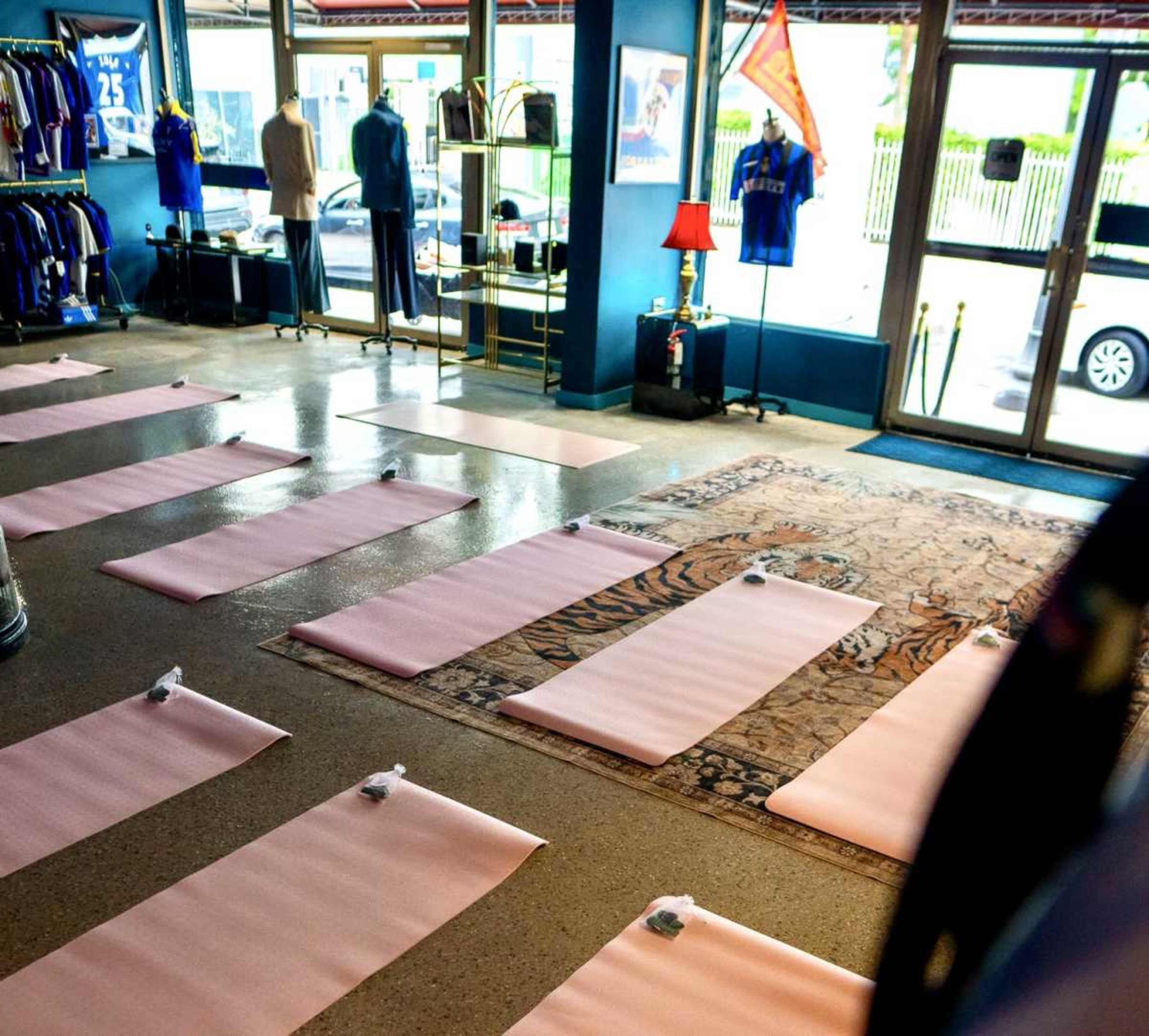 The image shows a room with several pink yoga mats arranged neatly on the floor, with displays of clothing and accessories visible in the background.