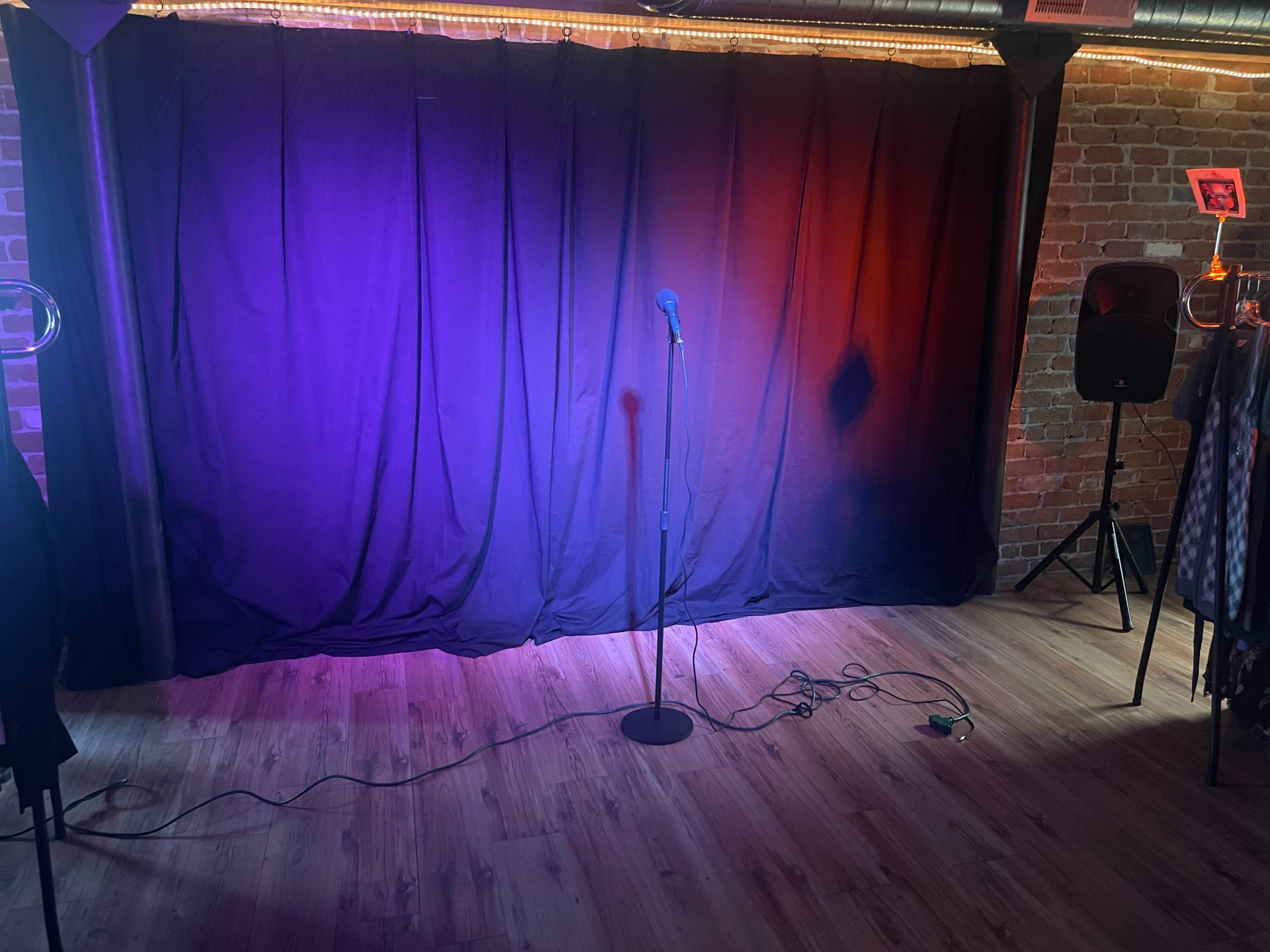 A microphone stands on a black stage in front of a dark curtain, with soft lighting illuminating the area.