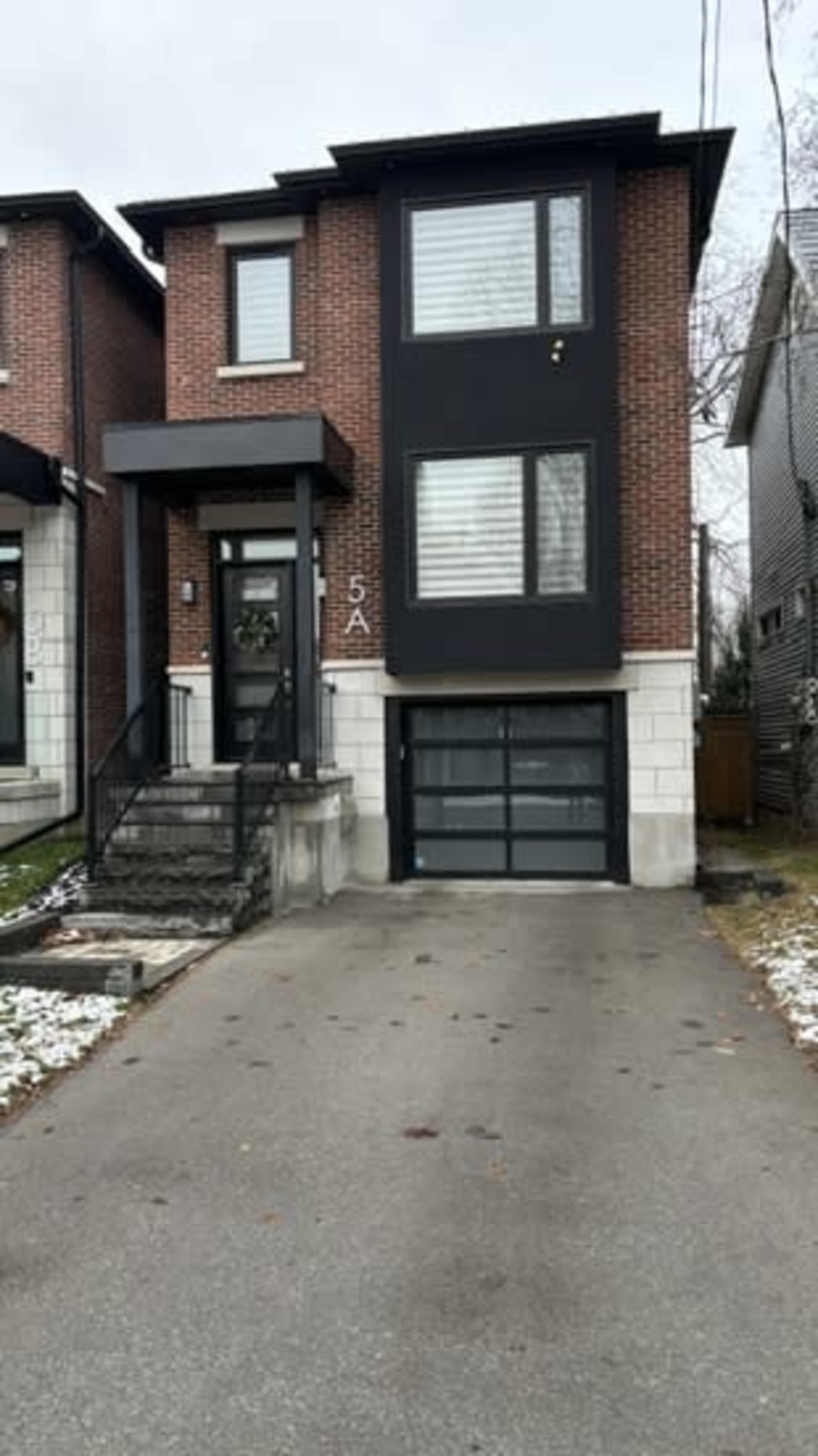 The image shows a modern two-story brick house with large windows, a garage, and a concrete walkway.