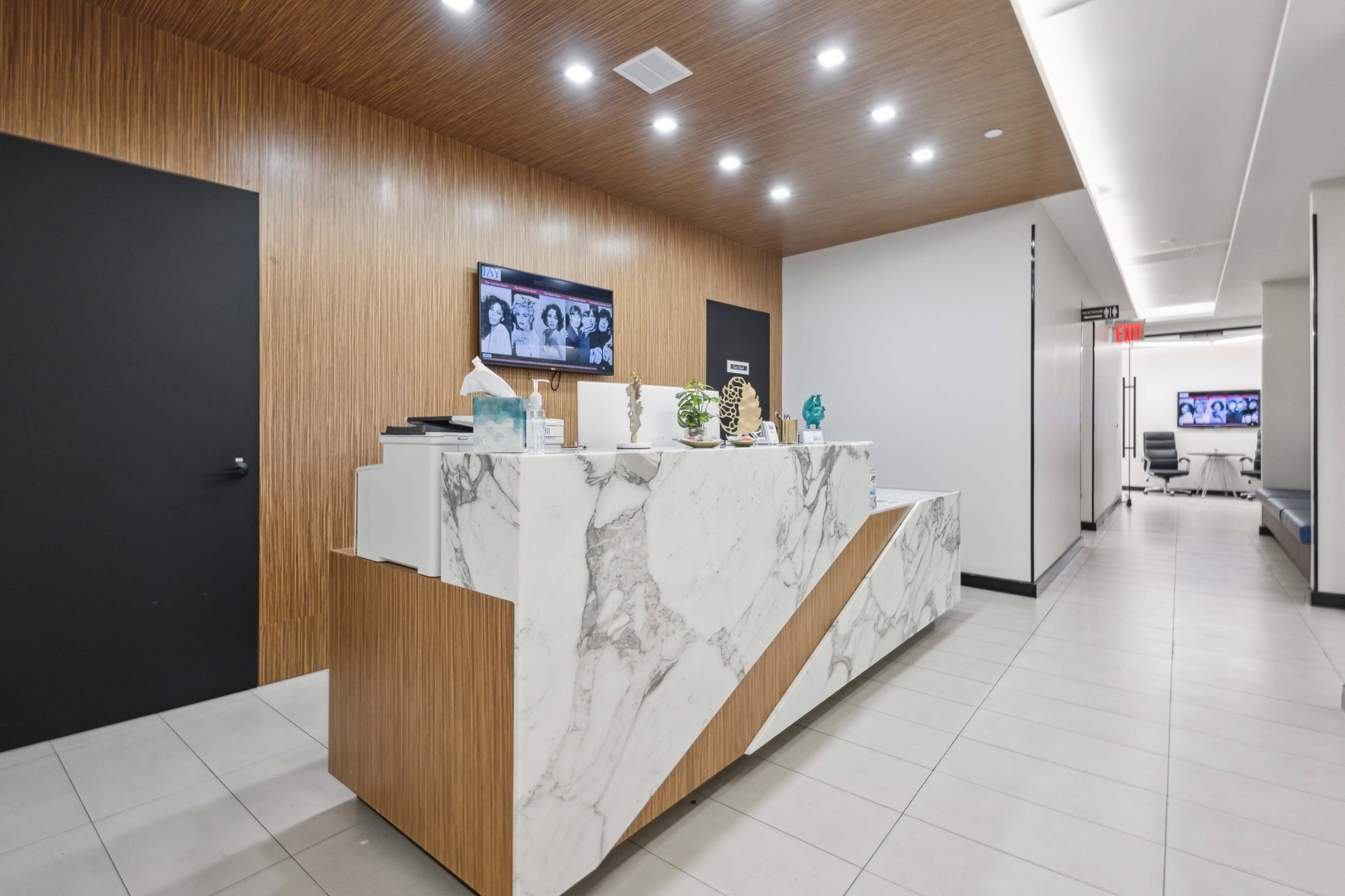 A modern reception area with a marble-front desk, wooden paneling on the walls, and a viewing screen displaying images.