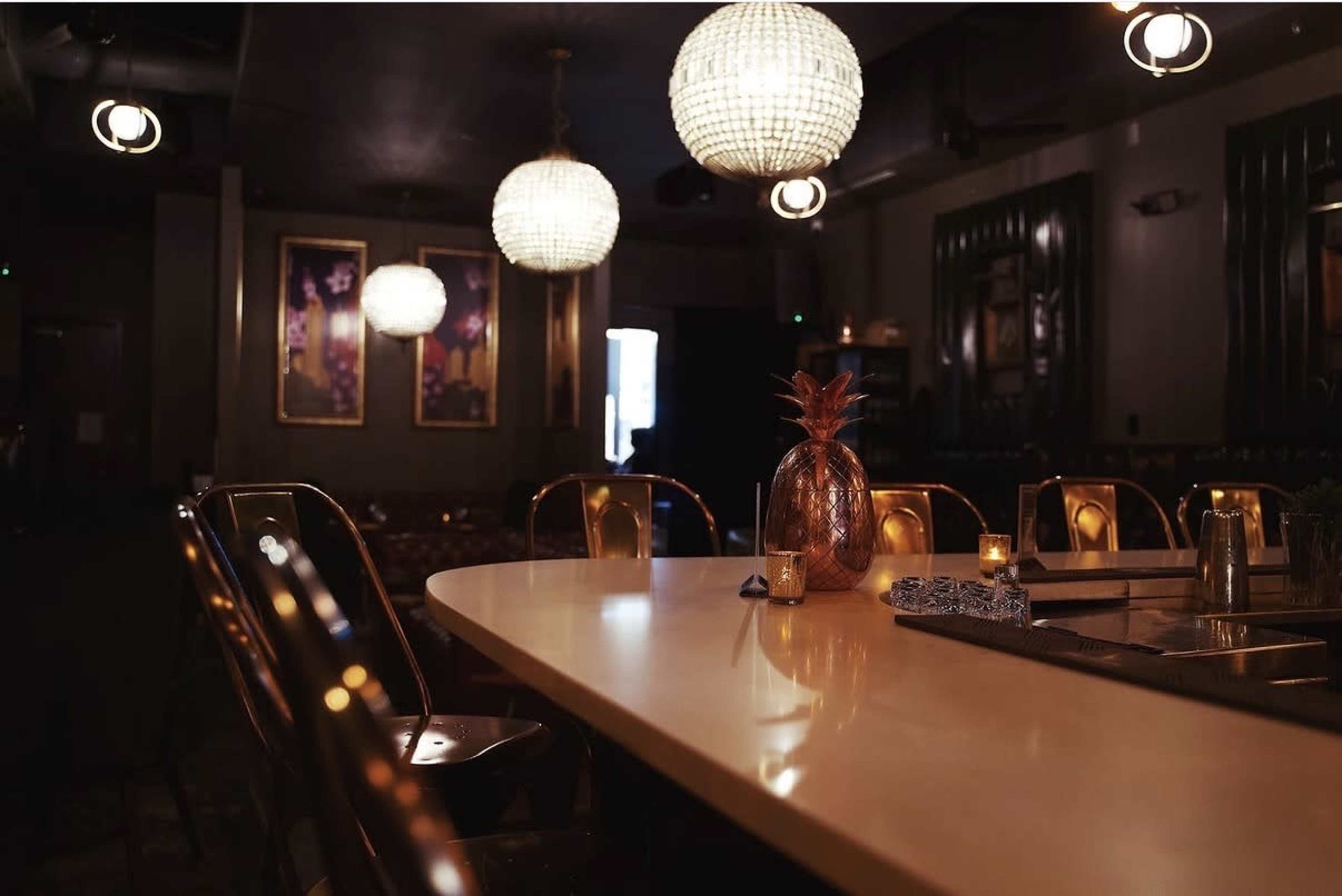 The image shows a dimly lit restaurant interior with a long table, elegant light fixtures, and a decorative pineapple centerpiece.