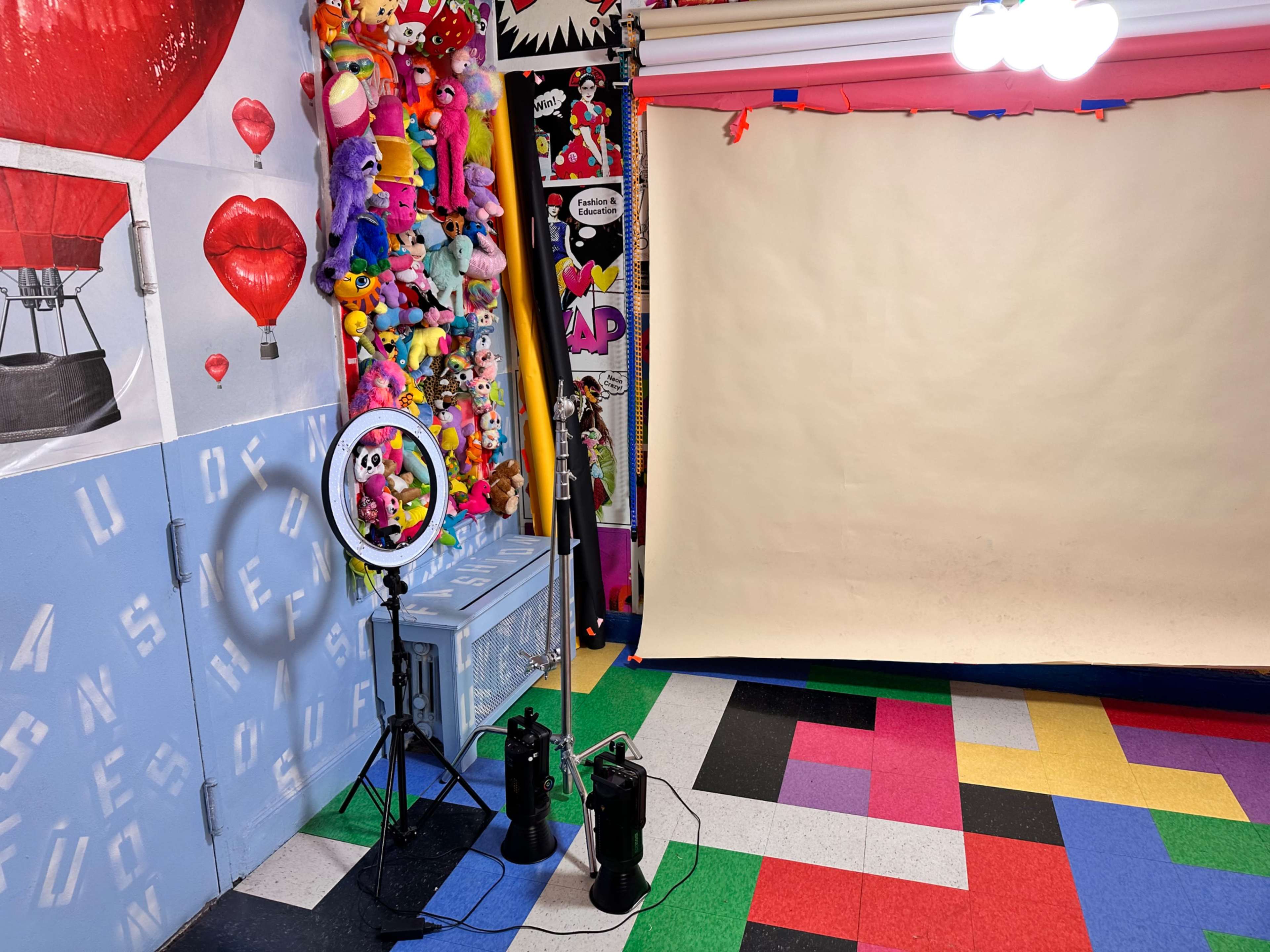 A colorful indoor photo studio with a blank backdrop, lighting equipment, and walls adorned with stuffed animals and decorations.
